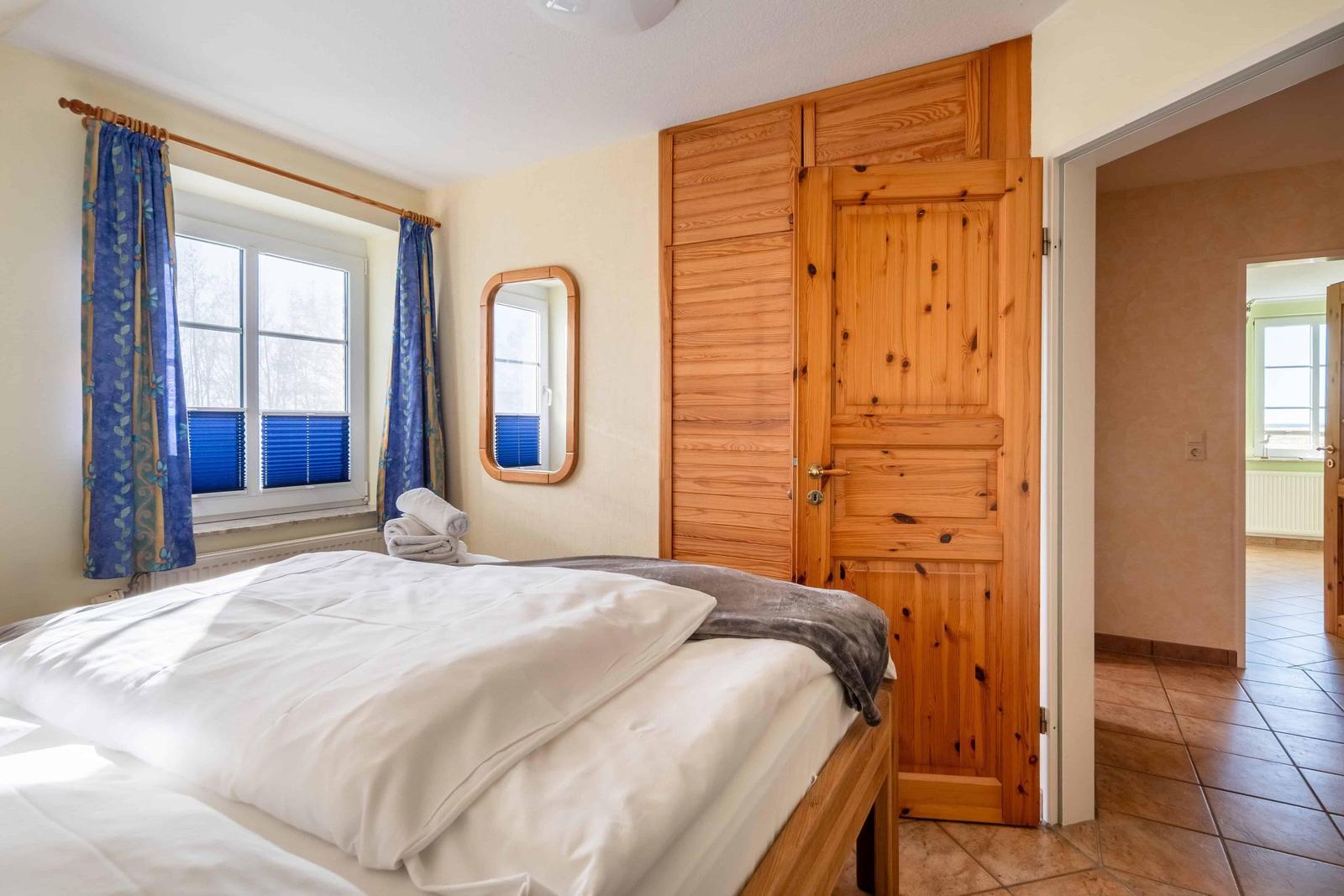 Schlafzimmer mit Bett, Holzschränk und Fenster mit blauen Vorhängen.