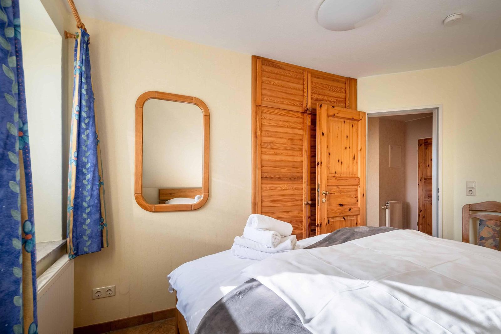 Schlafzimmer mit Bett, Holzschrank und Spiegel an der Wand.