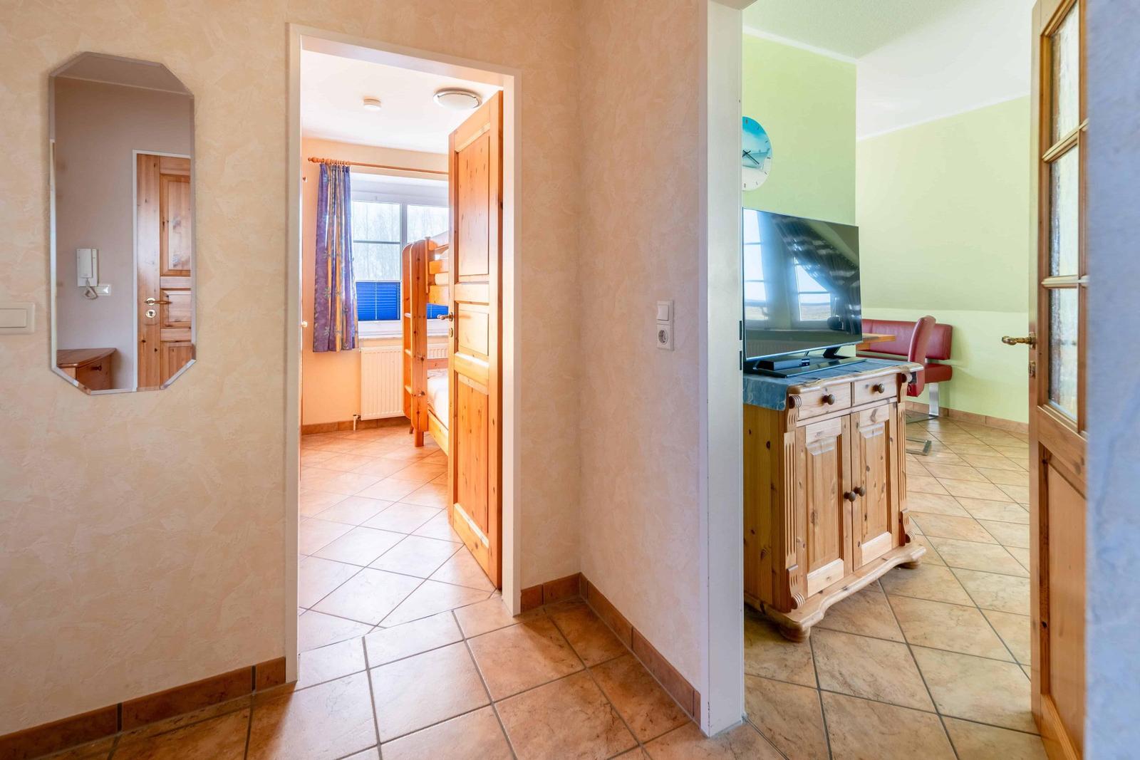 Hausflur mit Tür zu Schlafzimmer und Wohnzimmer mit Fernseher und Holzschrank.