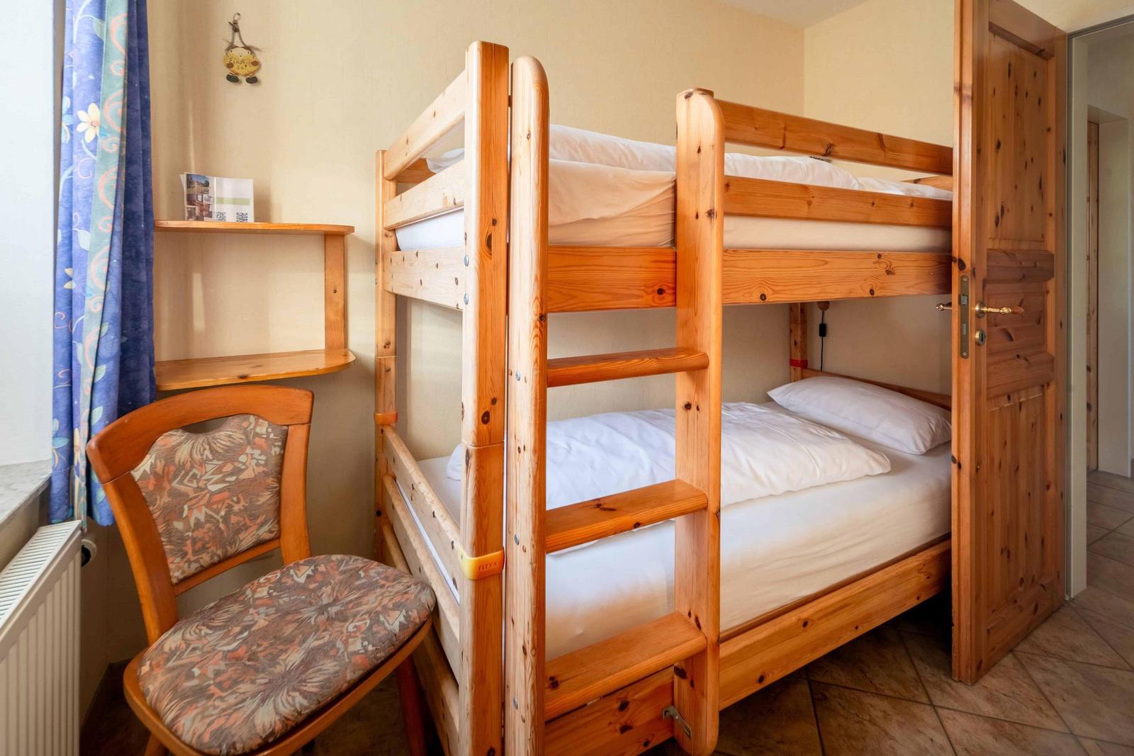 Ein Raum mit Holz-Etagenbett, Stuhl und Fenster mit Vorhang.