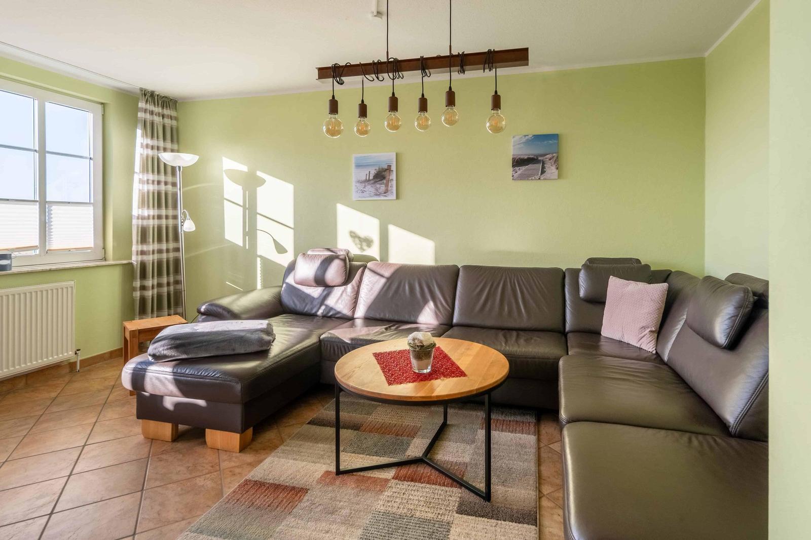 Wohnzimmer mit L-Förmigem Sofa, runden Tisch und hängenden Lampen.
