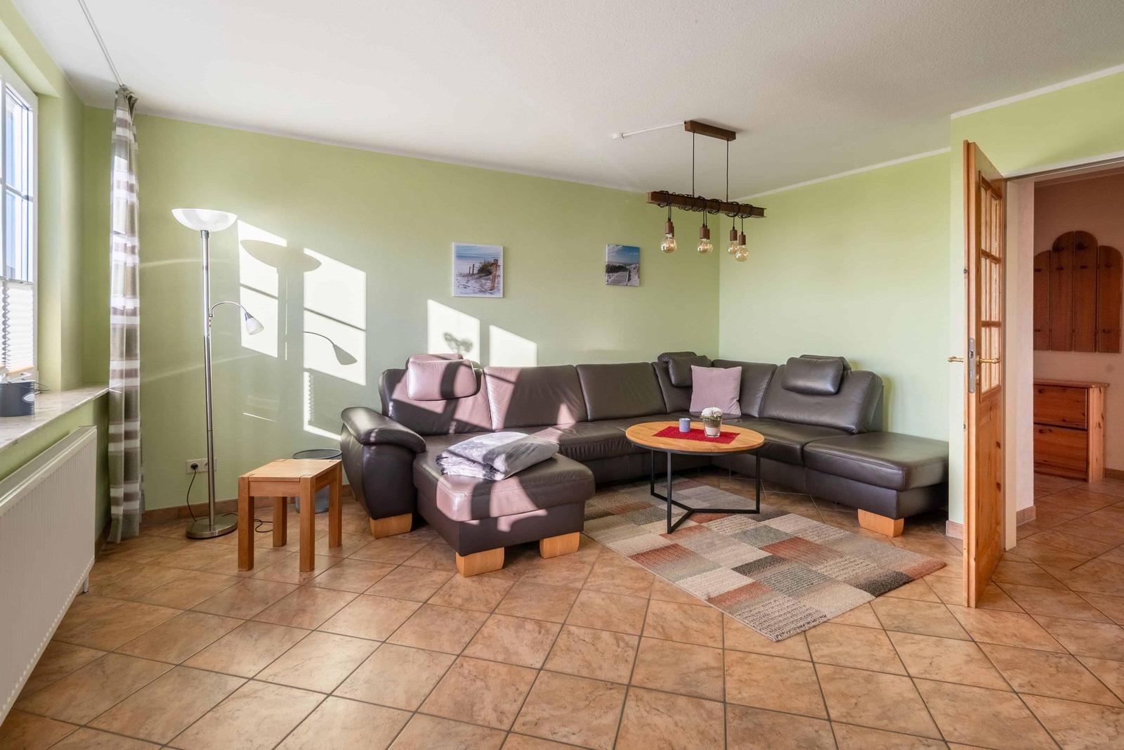 Wohnzimmer mit L-förmigem Sofa, runden Tisch und Holzboden.