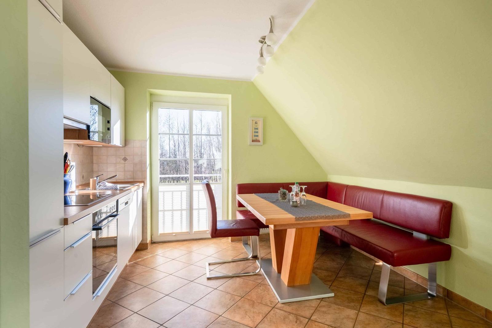 Küche mit Essbereich, rote Ledersitze, Holztisch, Fenster zur Terrasse.