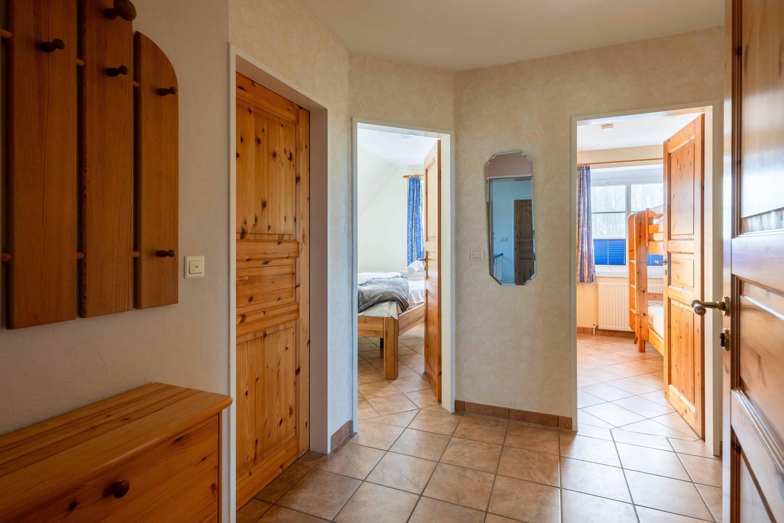 Flur mit Holztüren und -möbeln. Blick in zwei Schlafzimmer mit Betten und Fenstern.