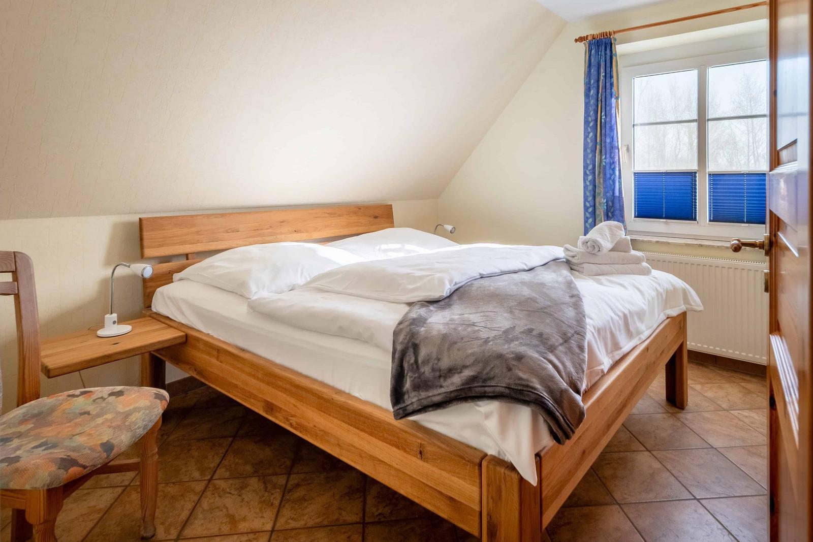 Ein Schlafzimmer mit Holzbett, Fenster mit blauen Vorhängen und gefliestem Boden.