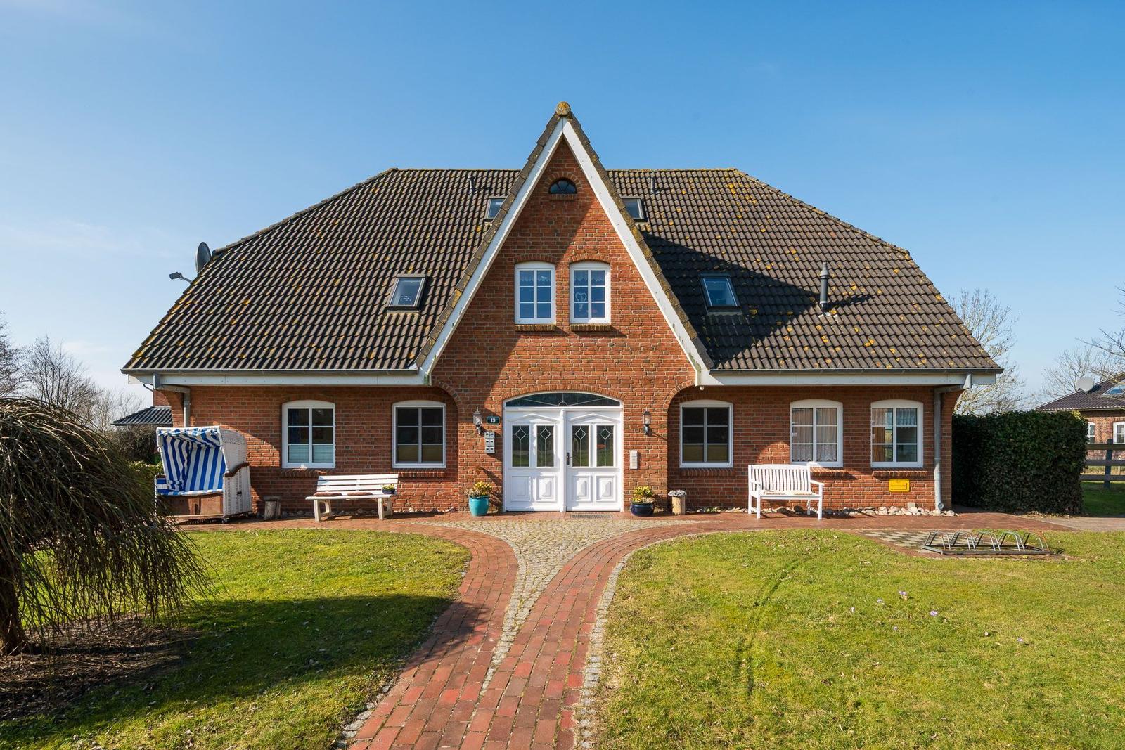 Red brick house with dormers and white door. Lawn and stone path in front.