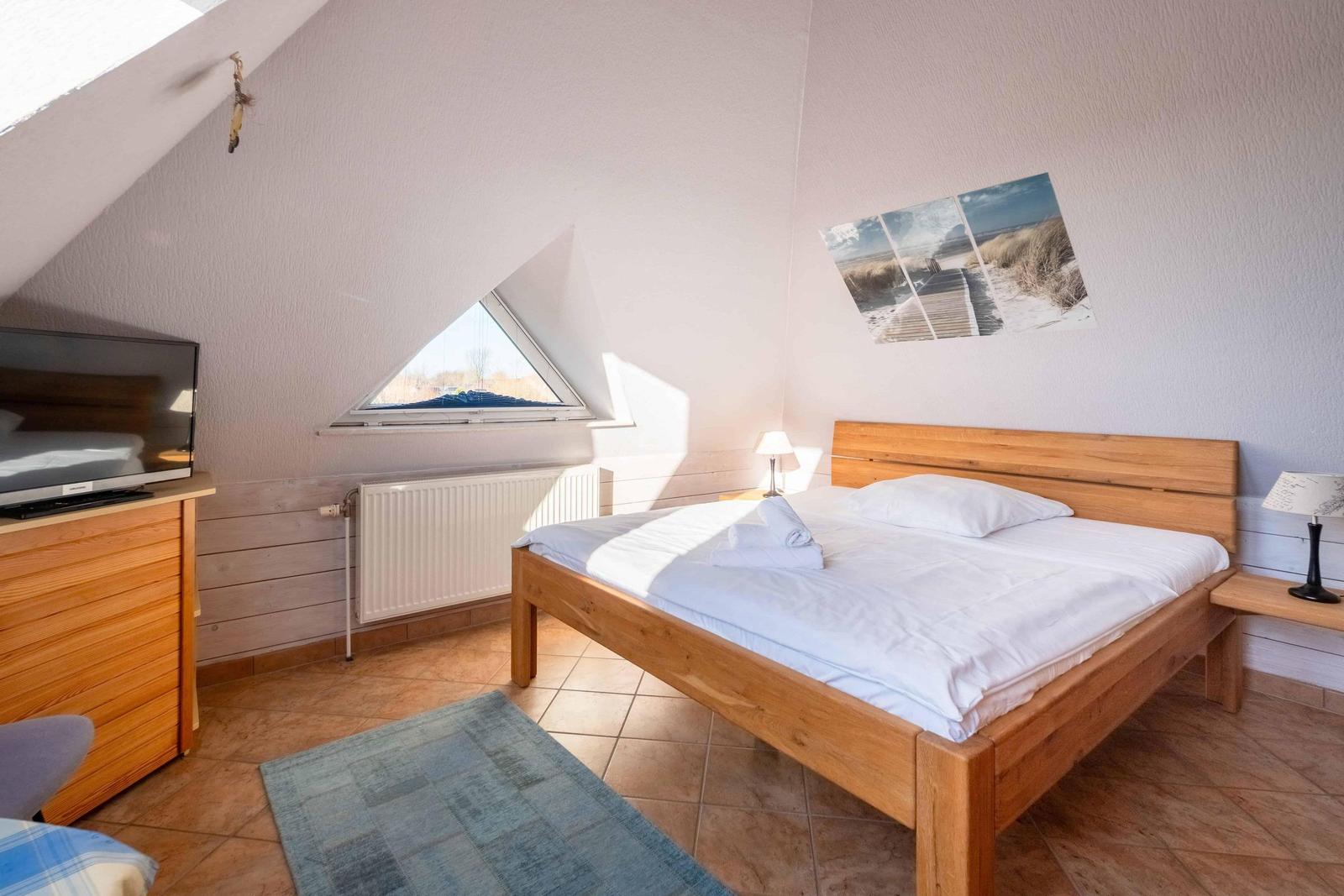 Bedroom with sloped ceiling, bed, TV, and window.