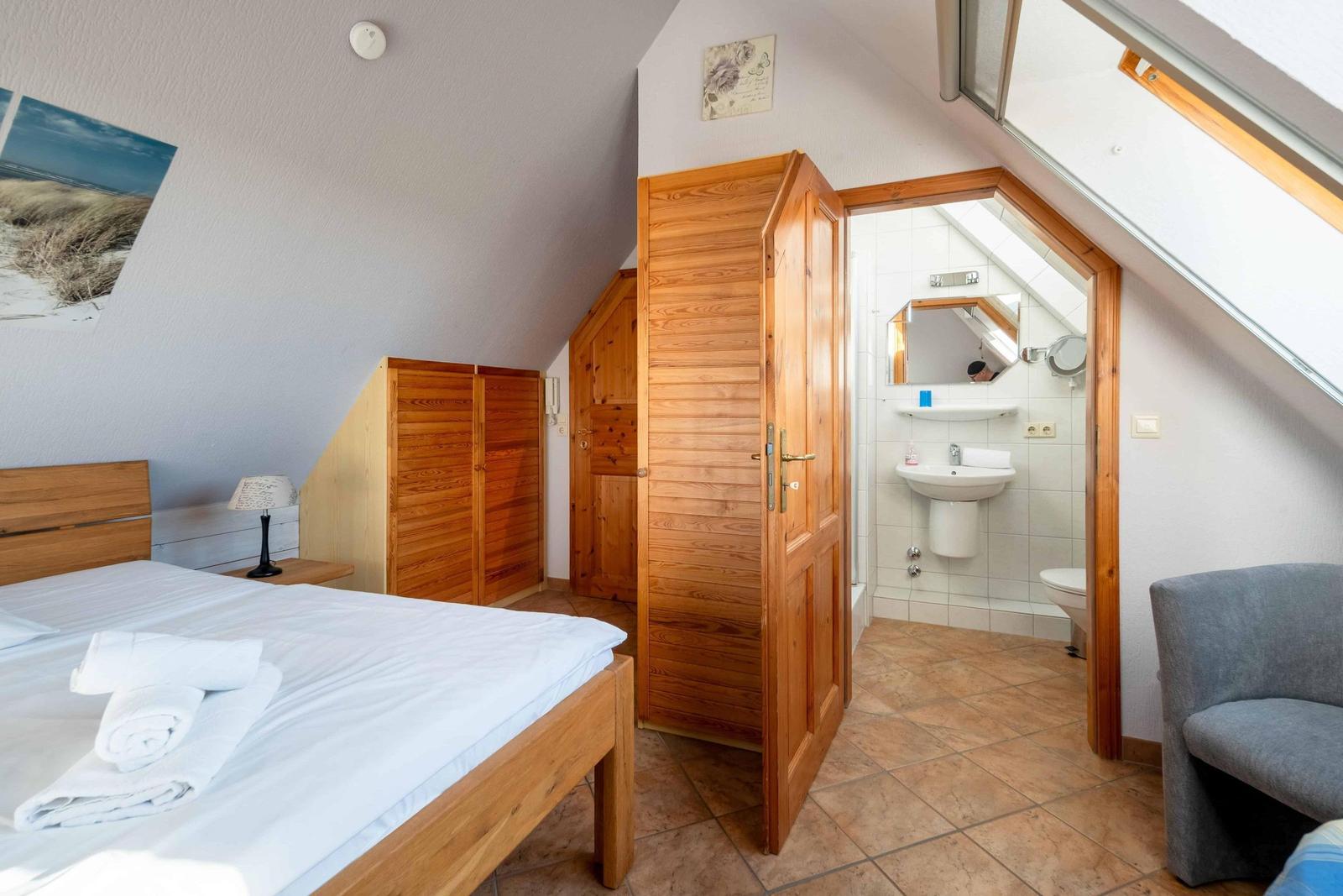 Bedroom with sloped ceiling, wooden bed, wardrobe, and adjacent toilet cubicle.