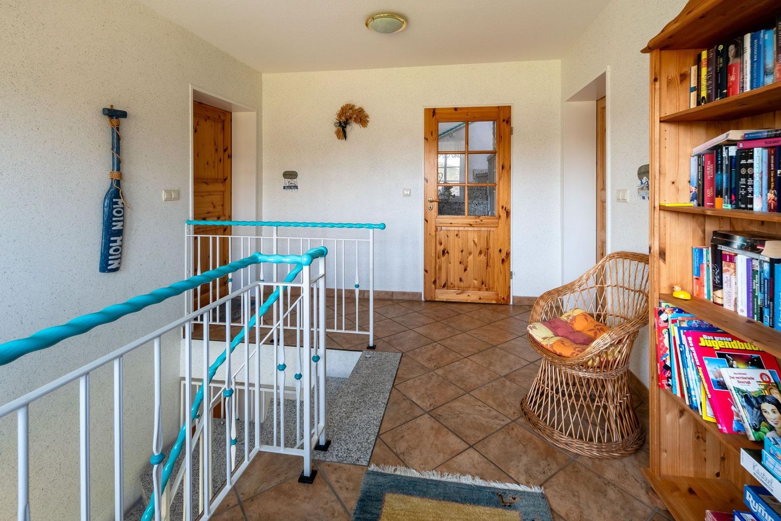 Entrance area with bookcase, wicker chair, and blue handrail.