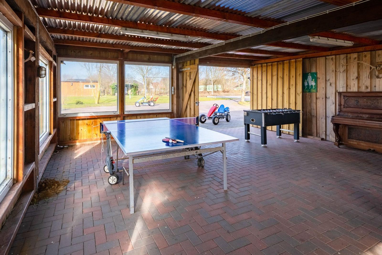 Game room with ping pong and foosball tables, wooden walls, and windows to outside view.