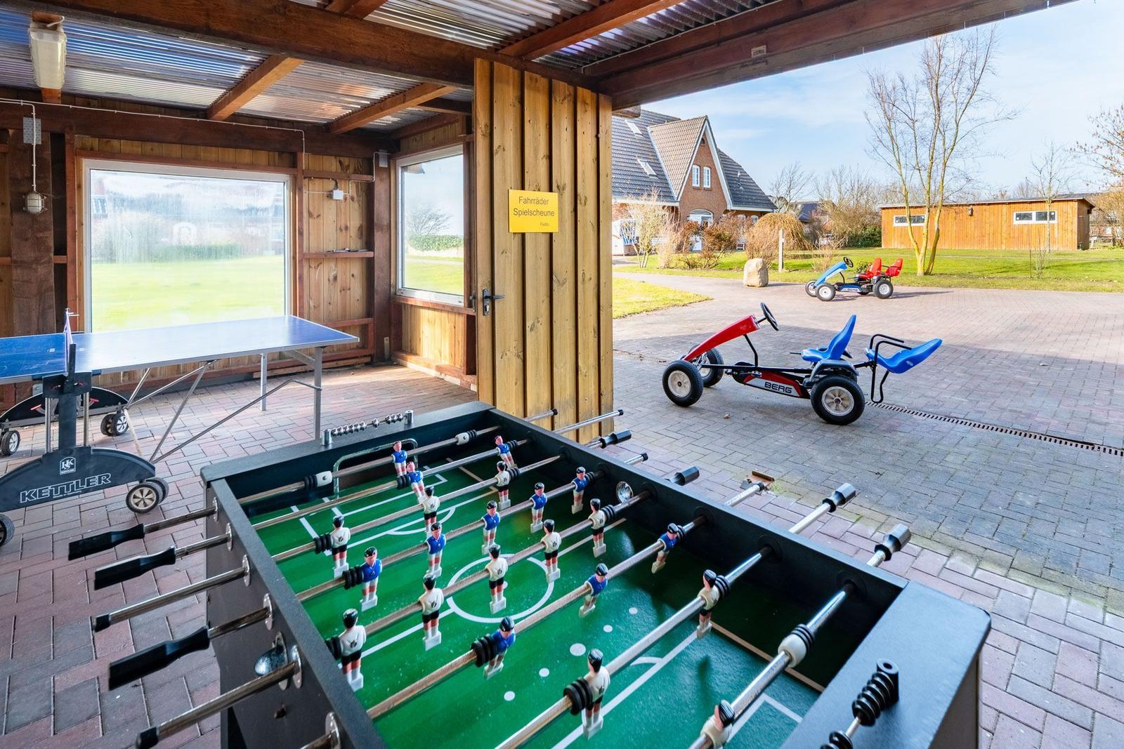 Foosball table and ping pong table in play area with childrens toys outside.