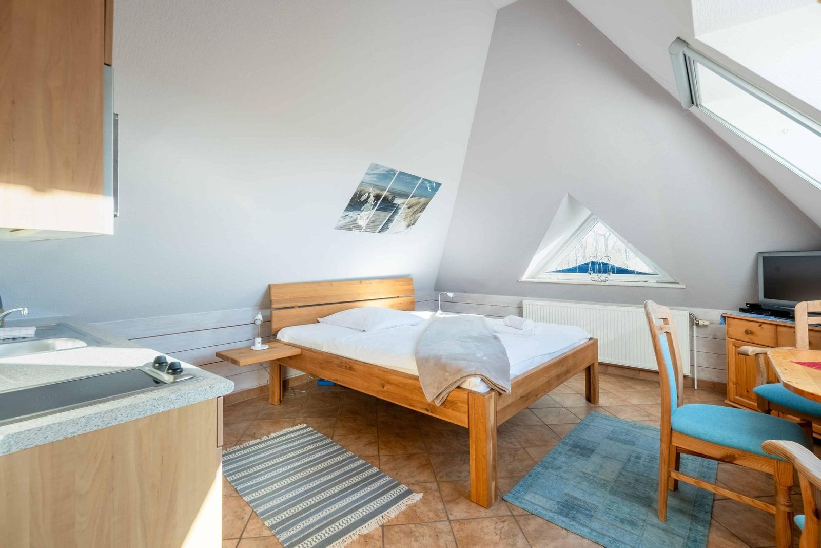 Schlafzimmer mit Doppelbett, Küchenzeile und Sitzgelegenheit unter Dachschrägen.