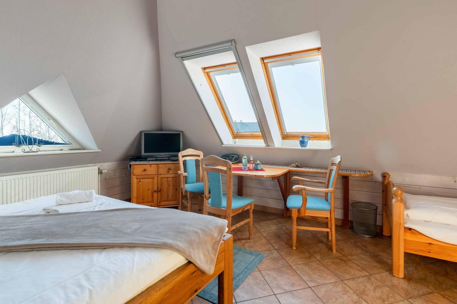 Zimmer mit Dachfenstern, Bett, Schlafcouch und Esstisch mit Stühlen.