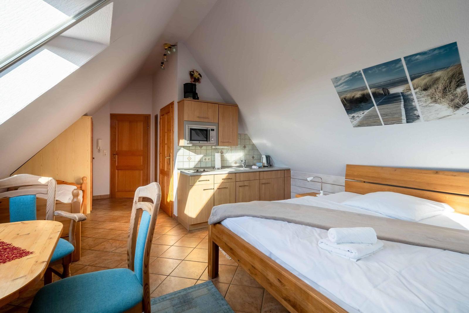 Schlafzimmer mit Doppelbett, Küchenzeile und Tisch mit Stühlen unter Dachschrägen.