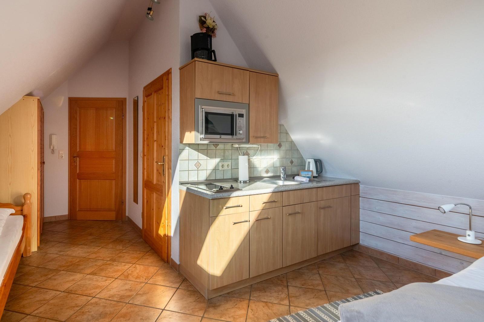 Küche mit Mikrowelle, Spüle und Kaffeemaschine in einem Schlafzimmer mit Holzboden und Dachschrägen.