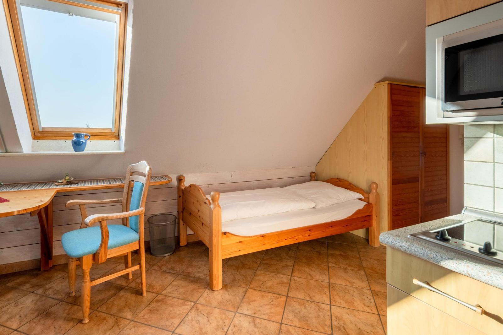 Zimmer mit Doppelbett, Schreibtisch, Stuhl und Küchenbereich mit Mikrowelle.
