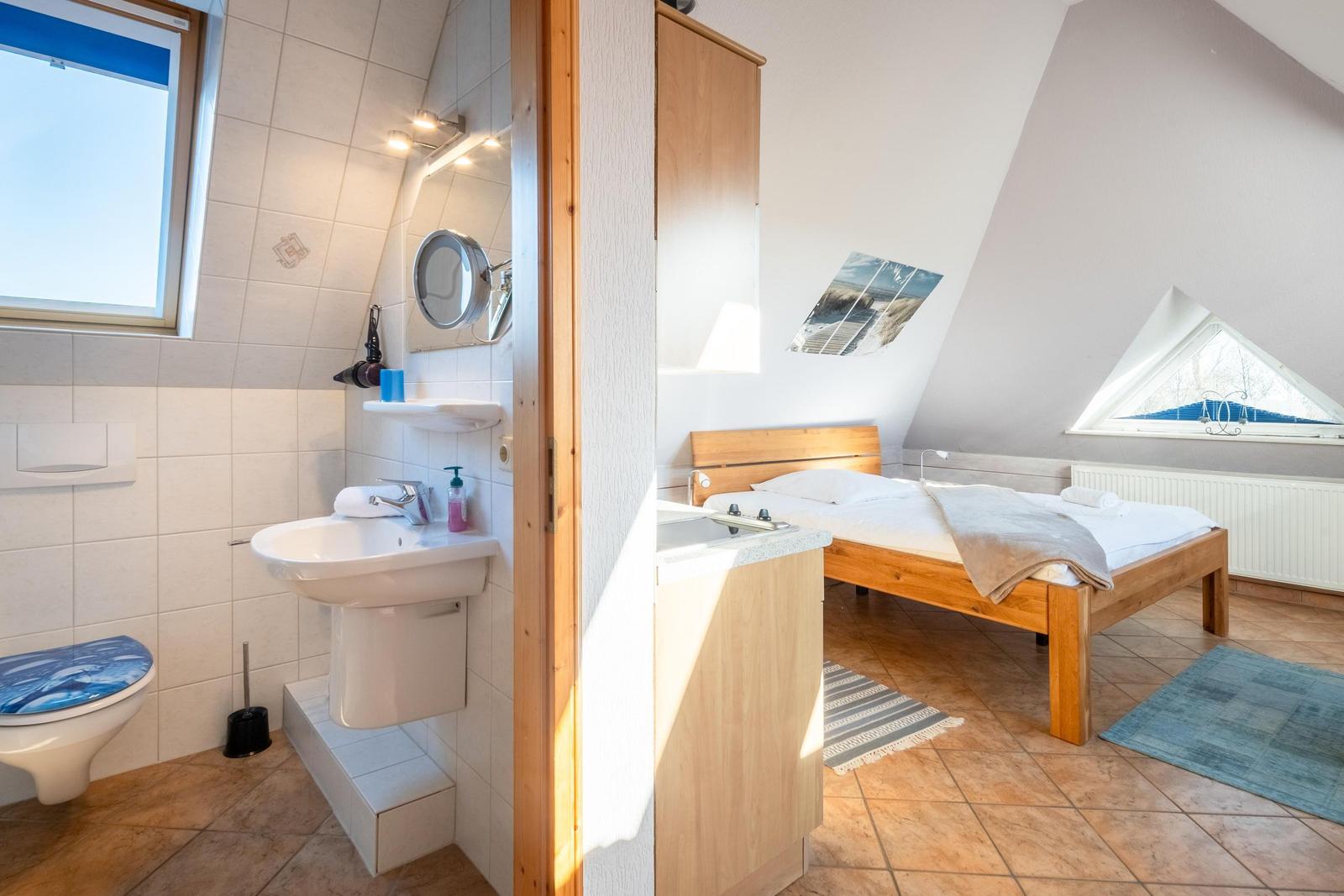 Schlafzimmer mit Holzbett und Dachfenster. Nebenraum mit Waschbecken und Toilette.