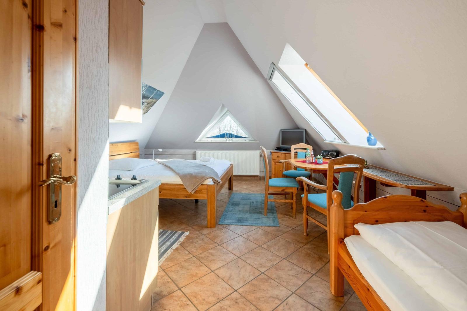 Schlafzimmer mit zwei Betten, Tisch und Stühlen unter Dachschrägen mit Fenstern.