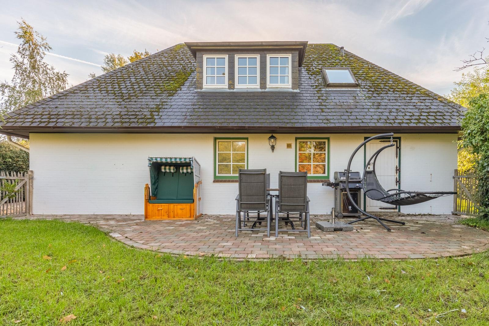 Wohnhaus mit Terrasse, Liege, Grill und Strandkorb. Grünfläche vor dem Haus.