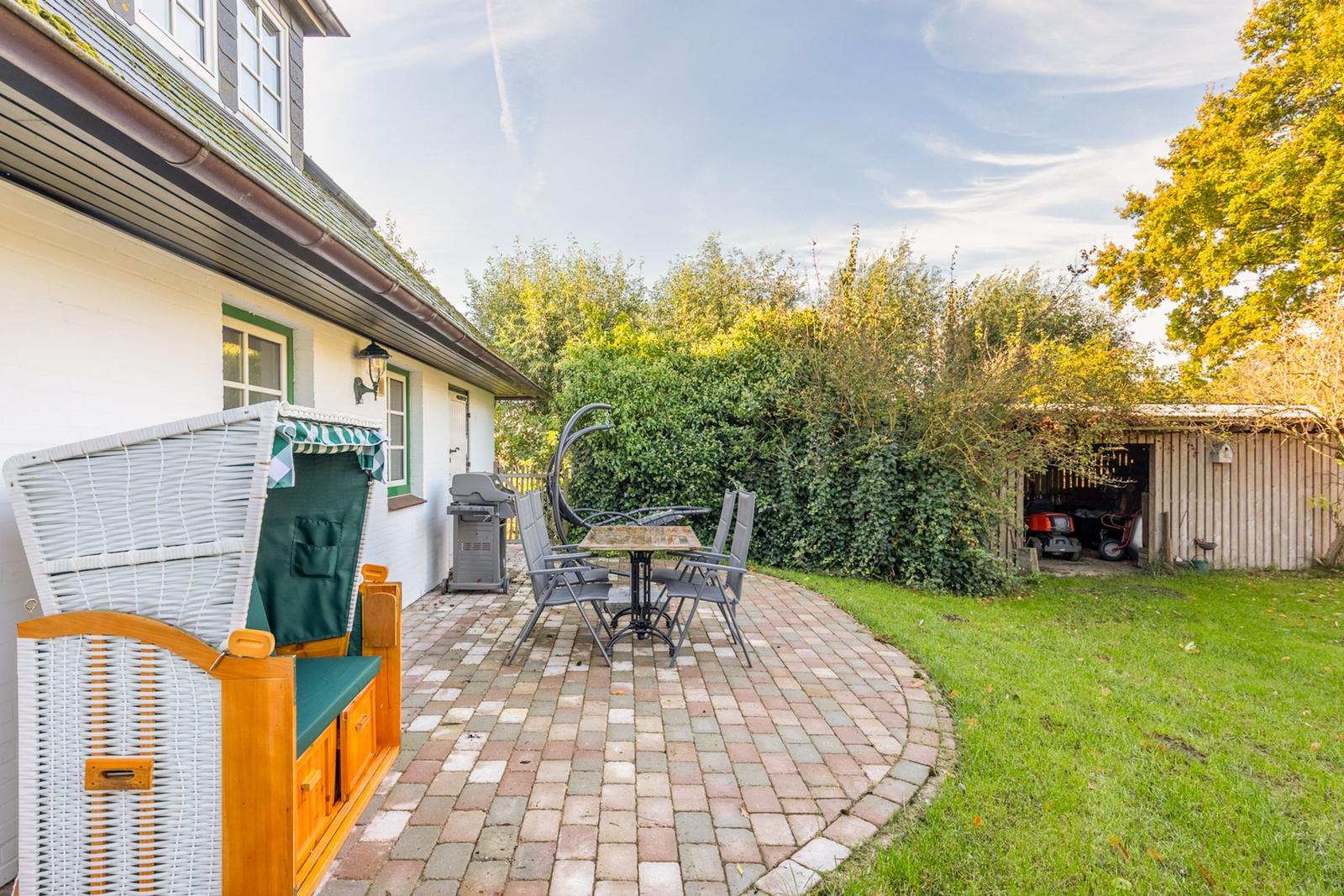 Hinterhof mit Terrasse, Grill und Liegestuhl. Grünflächen und Hecke im Hintergrund.