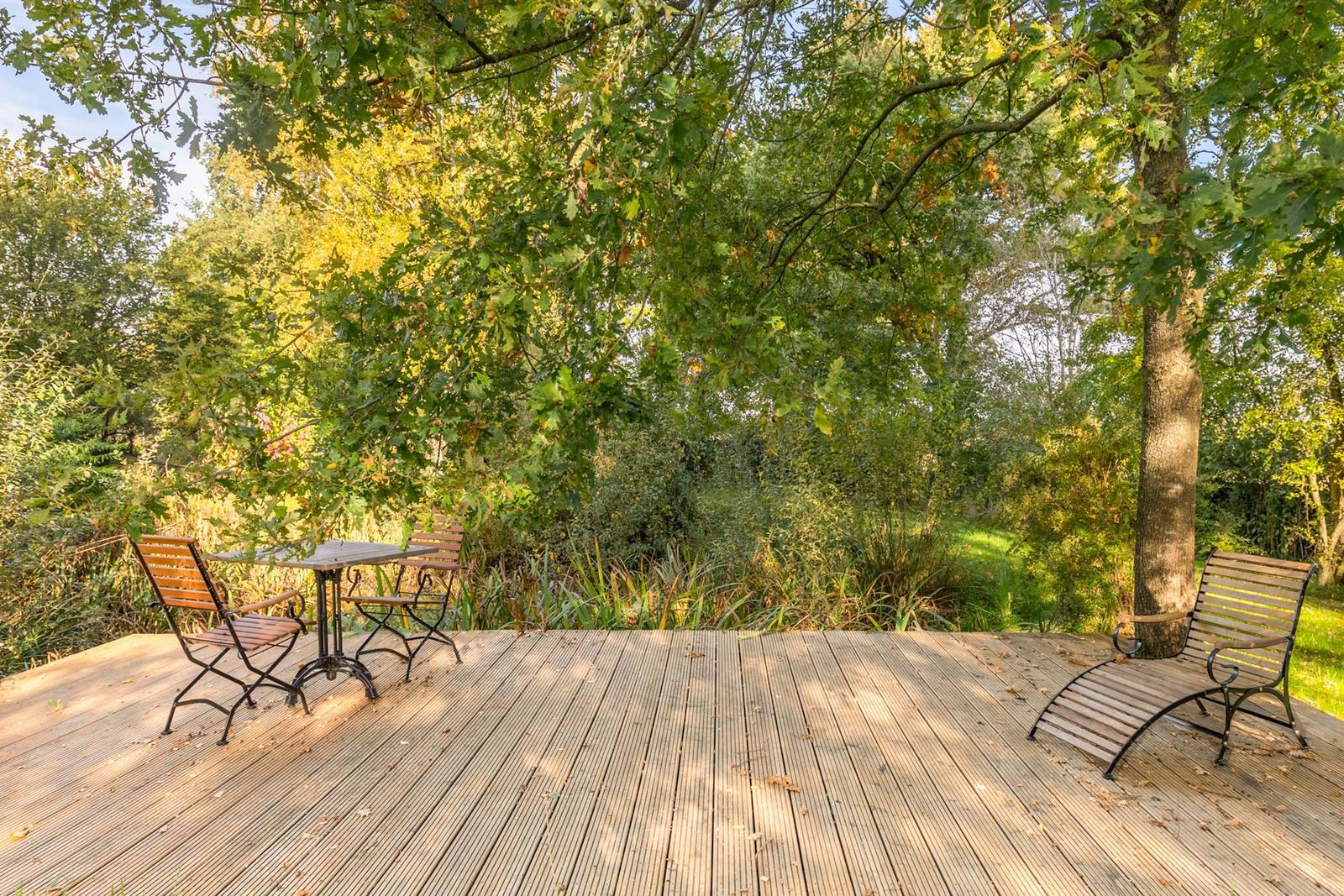 Holzterrasse mit Tisch und Stühlen unter Bäumen. Natürlicher Gartenblick.