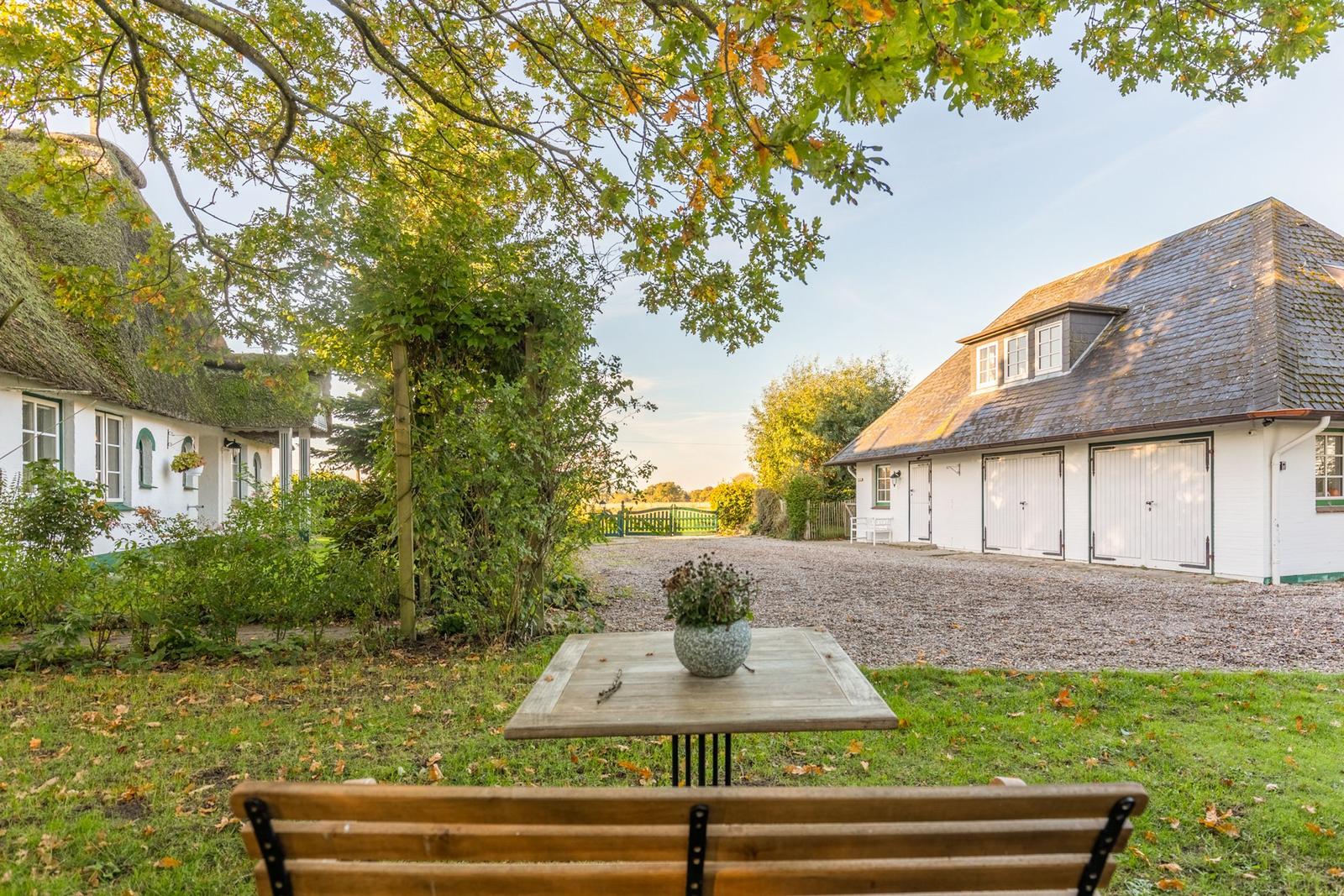 Haus mit Strohdach und Garage im Grünen. Tisch und Bank im Vorgarten.