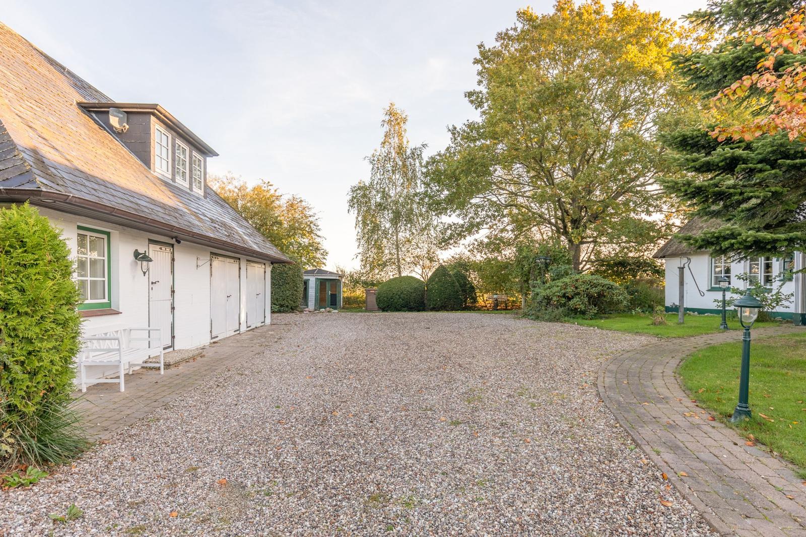 Haus mit Kiesfläche, Grünflächen und Bäumen im Herbstlicht.