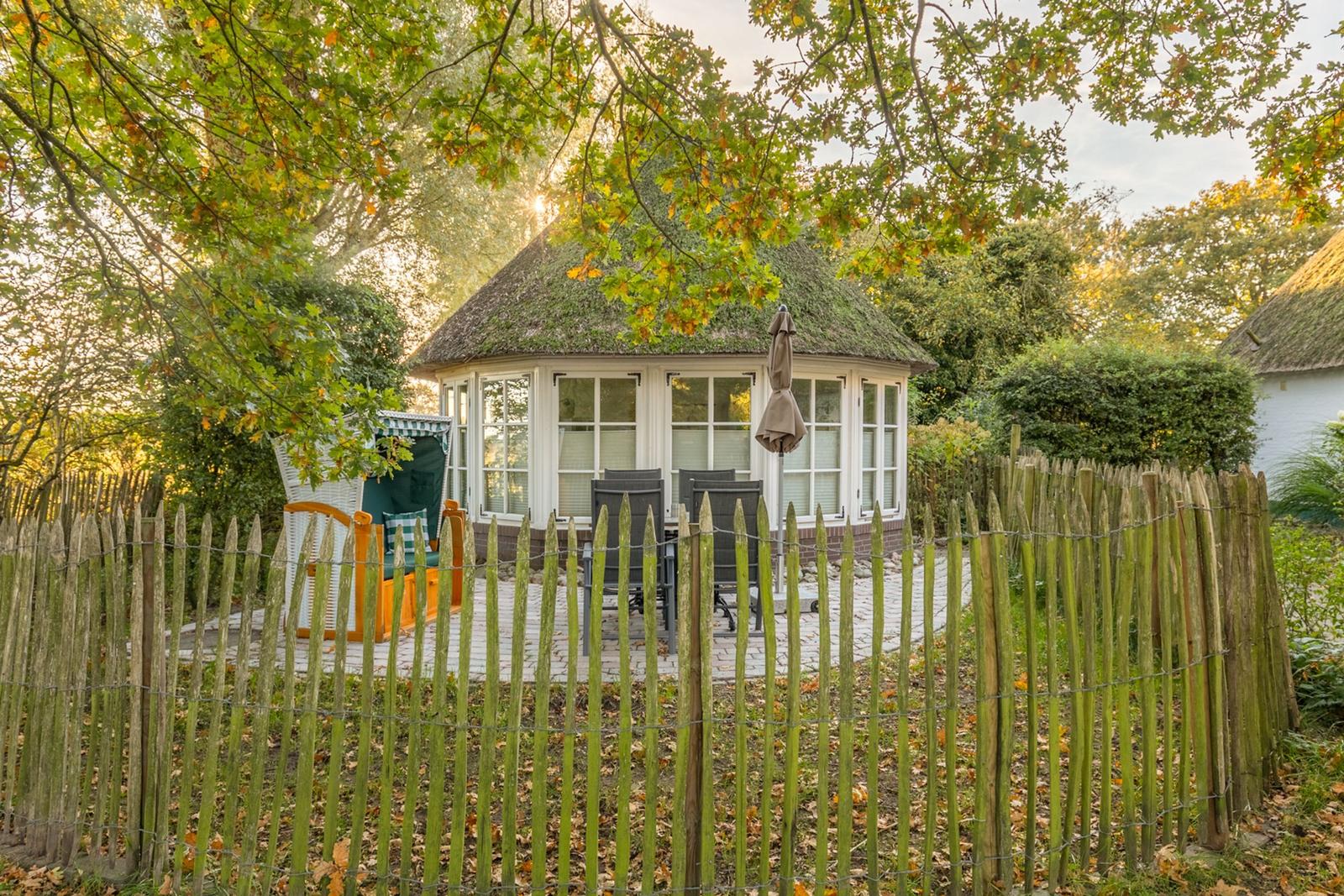 Ein weißes Haus mit strohgedecktem Dach und großem Fensterbereich im Garten.