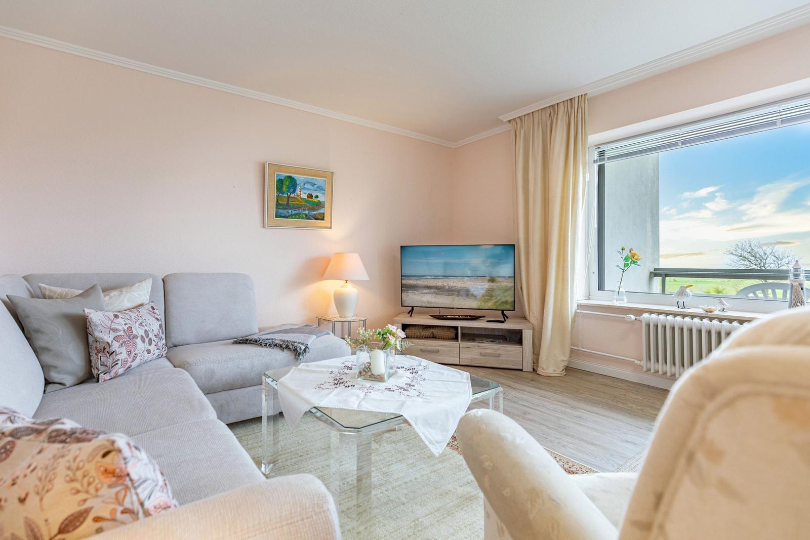 Wohnzimmer mit Sofa, Fernseher und großem Fenster mit Blick auf Landschaft.