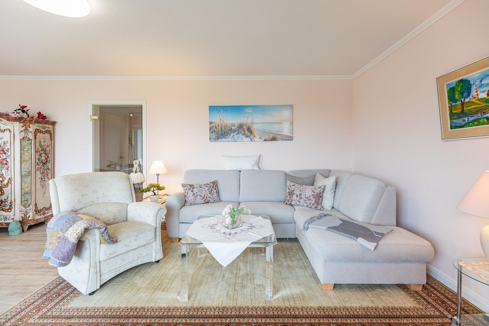Wohnzimmer mit Ecksofa, Sessel, Glas-Tisch und Wandbild.