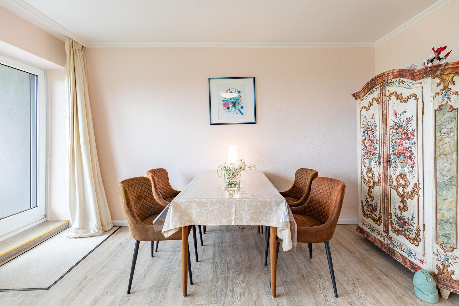 Esszimmer mit Tisch, vier Stühlen, Wandbild und dekorativem Schrank.