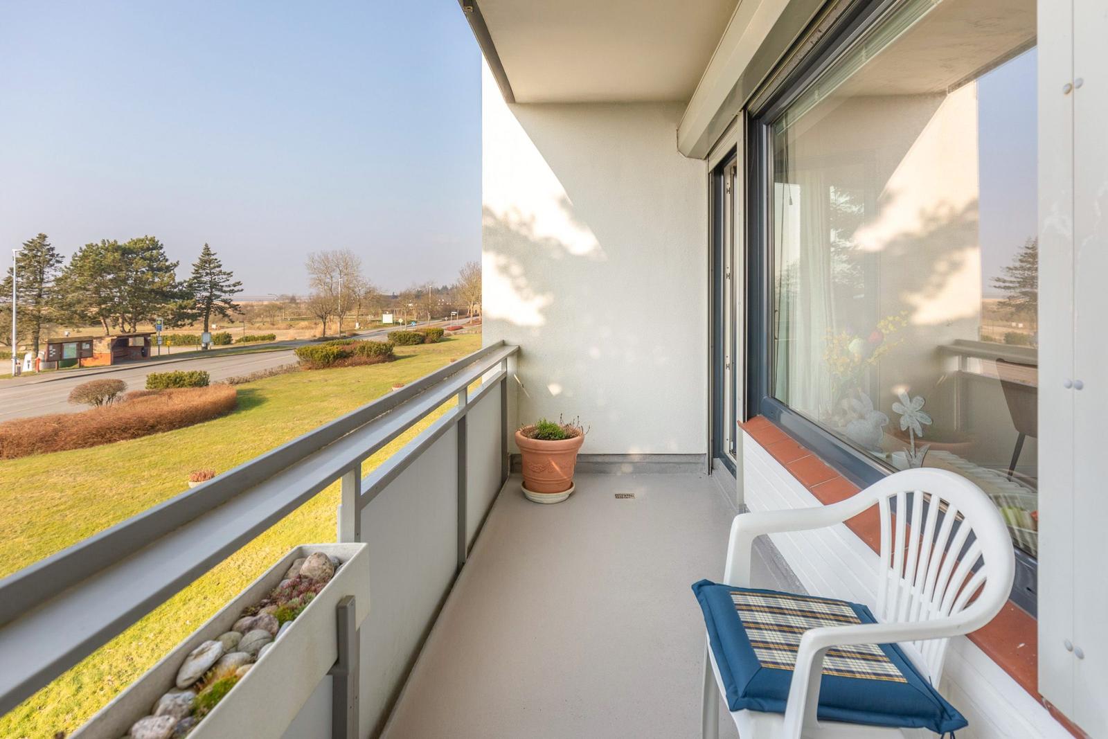 Balkon mit Stuhl, Pflanze und Blick auf Grünfläche und Straße.