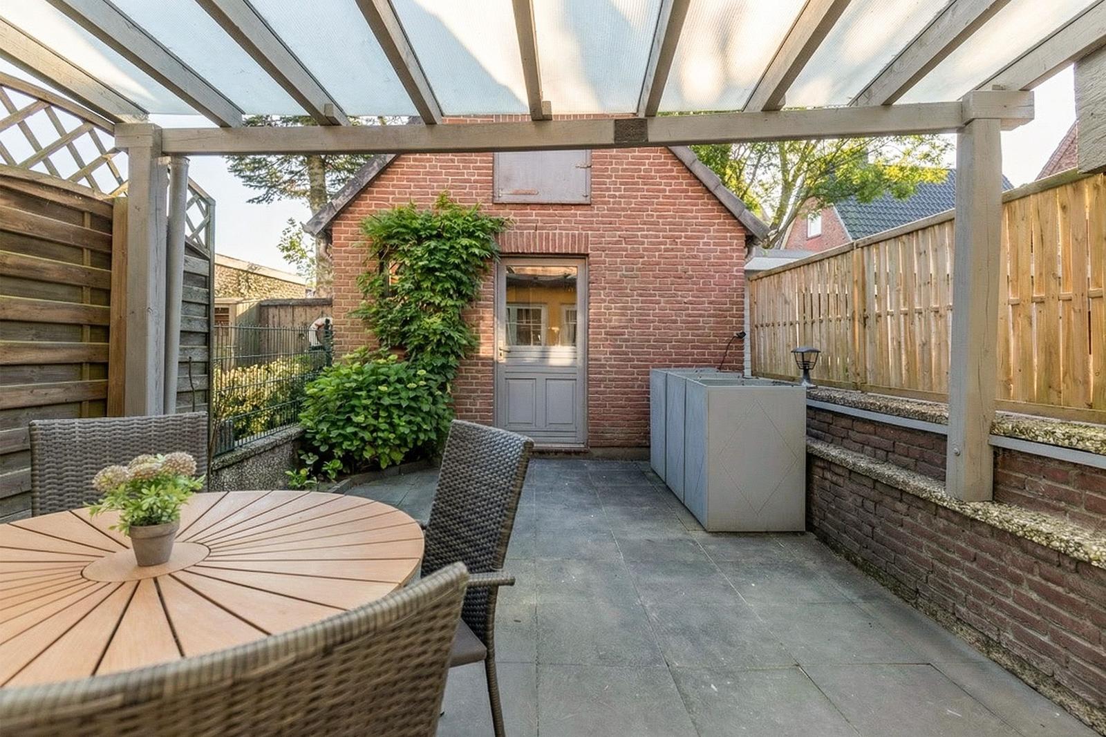 Terrasse mit Pavillon, Tisch und Stühlen. Hinterhof mit Backsteinmauer und Pflanzen.