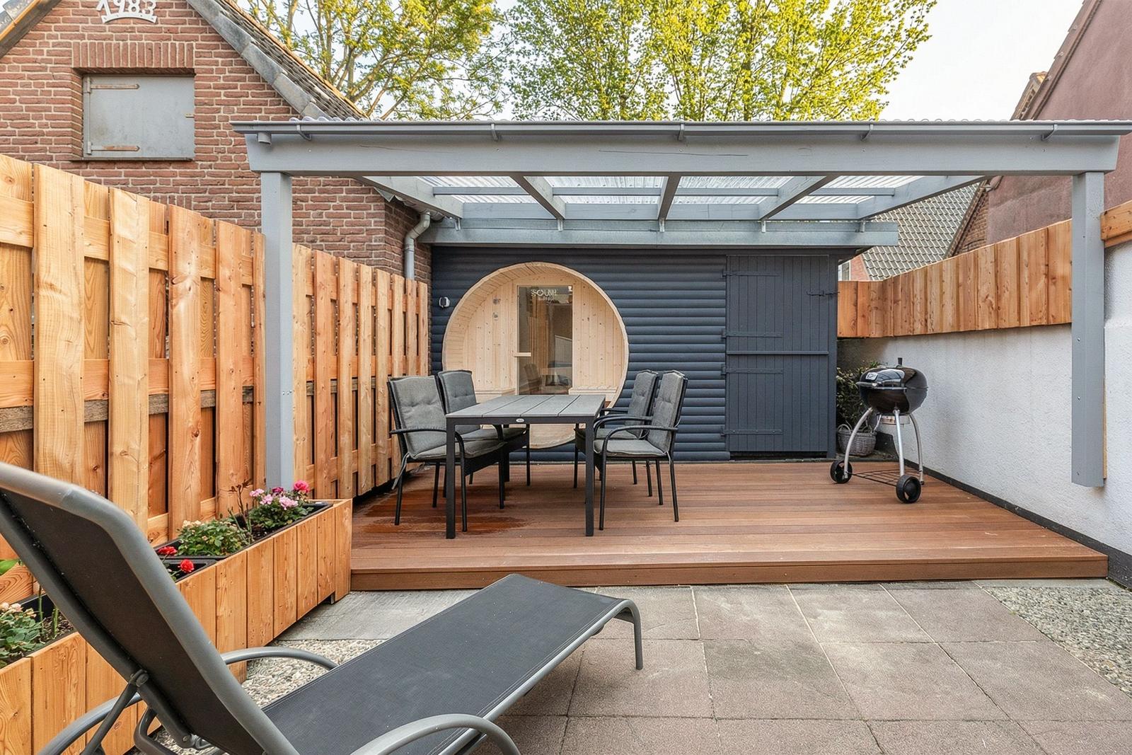 Terrasse mit Sitzgruppe, Grill und Holzdecke. Runder Holzaufbau im Hintergrund.