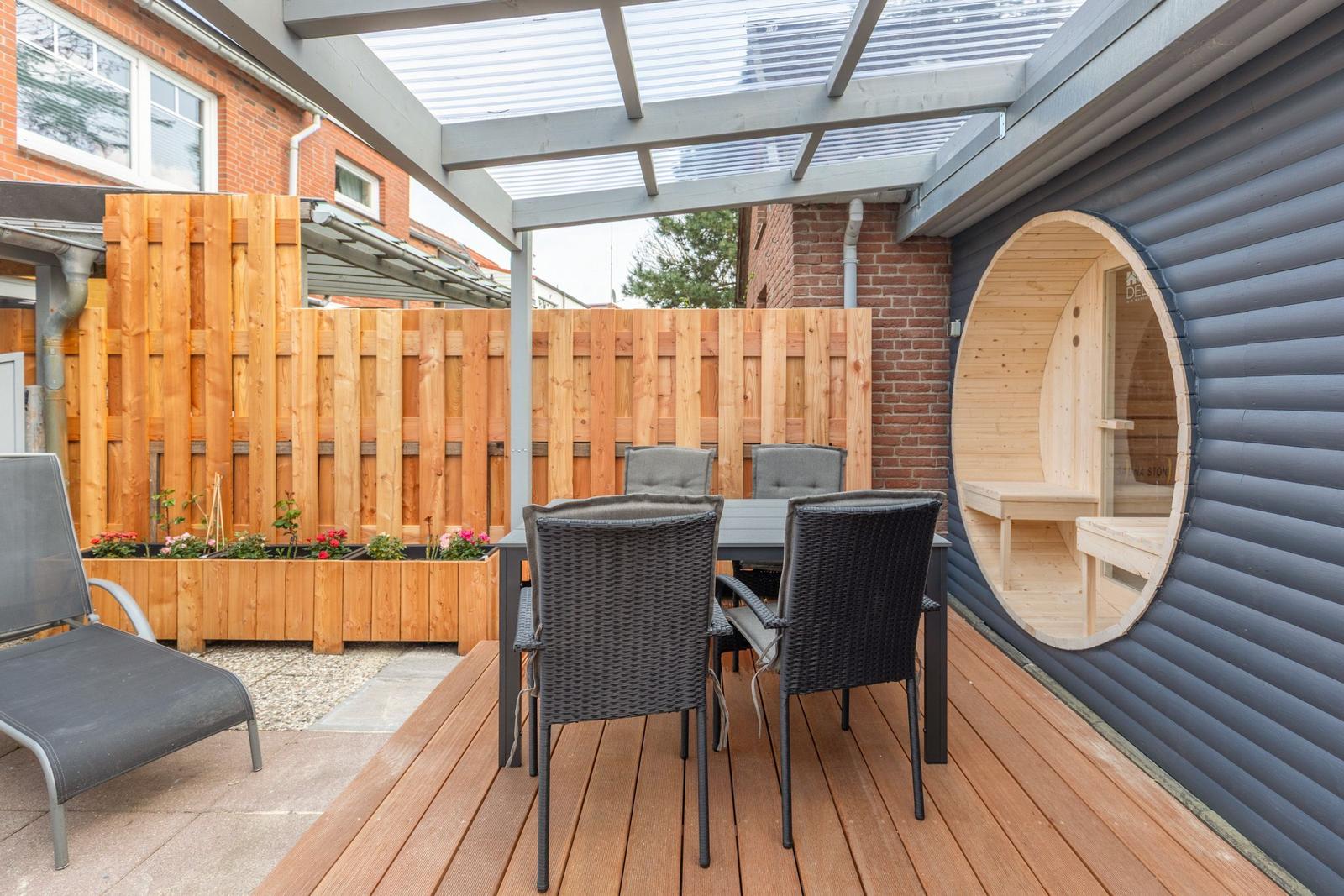Terrasse mit Sitzgruppe, Holzdecke und runder Saunaöffnung an der Wand.
