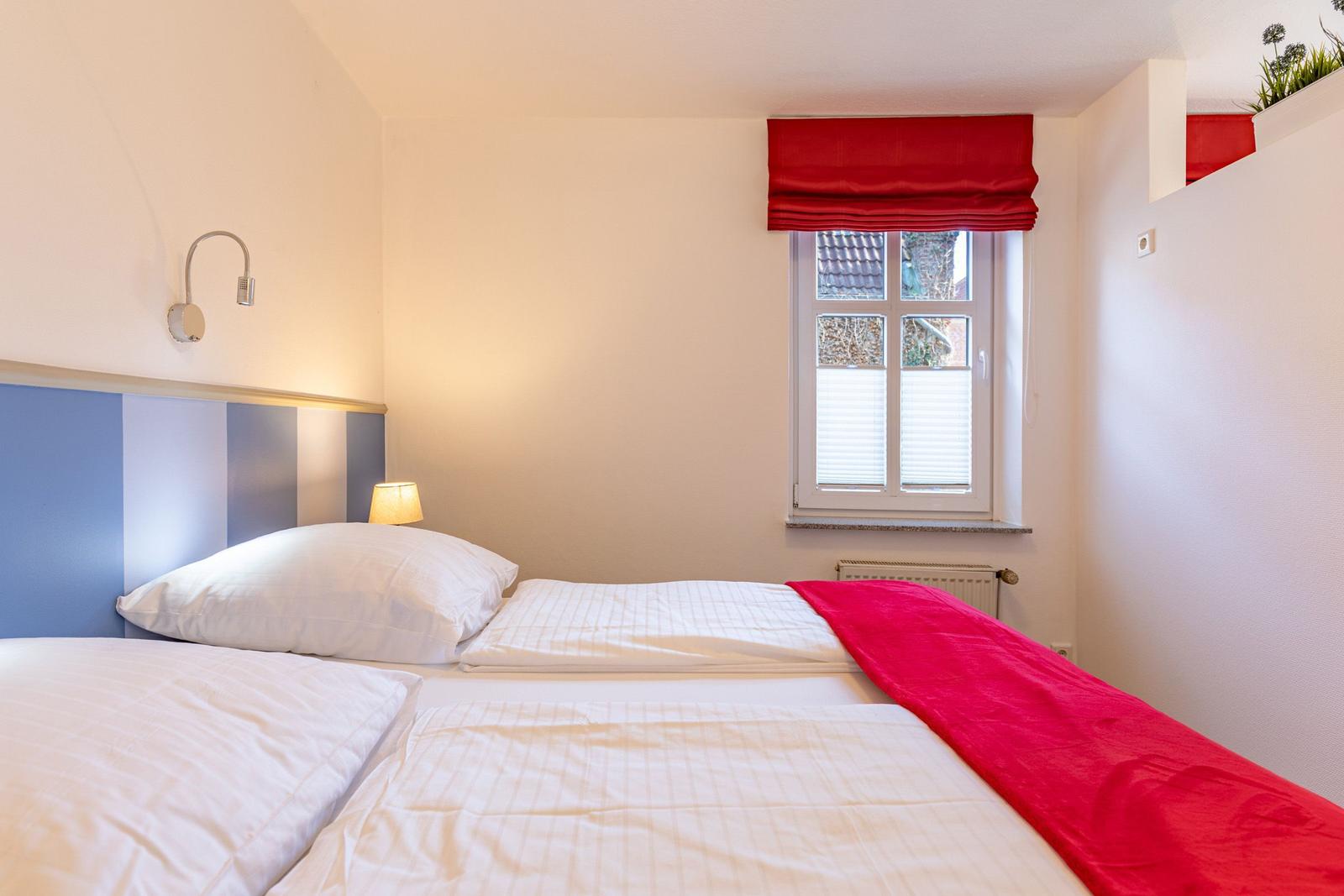 Schlafzimmer mit Bett, Fenster und rotem Vorhang.
