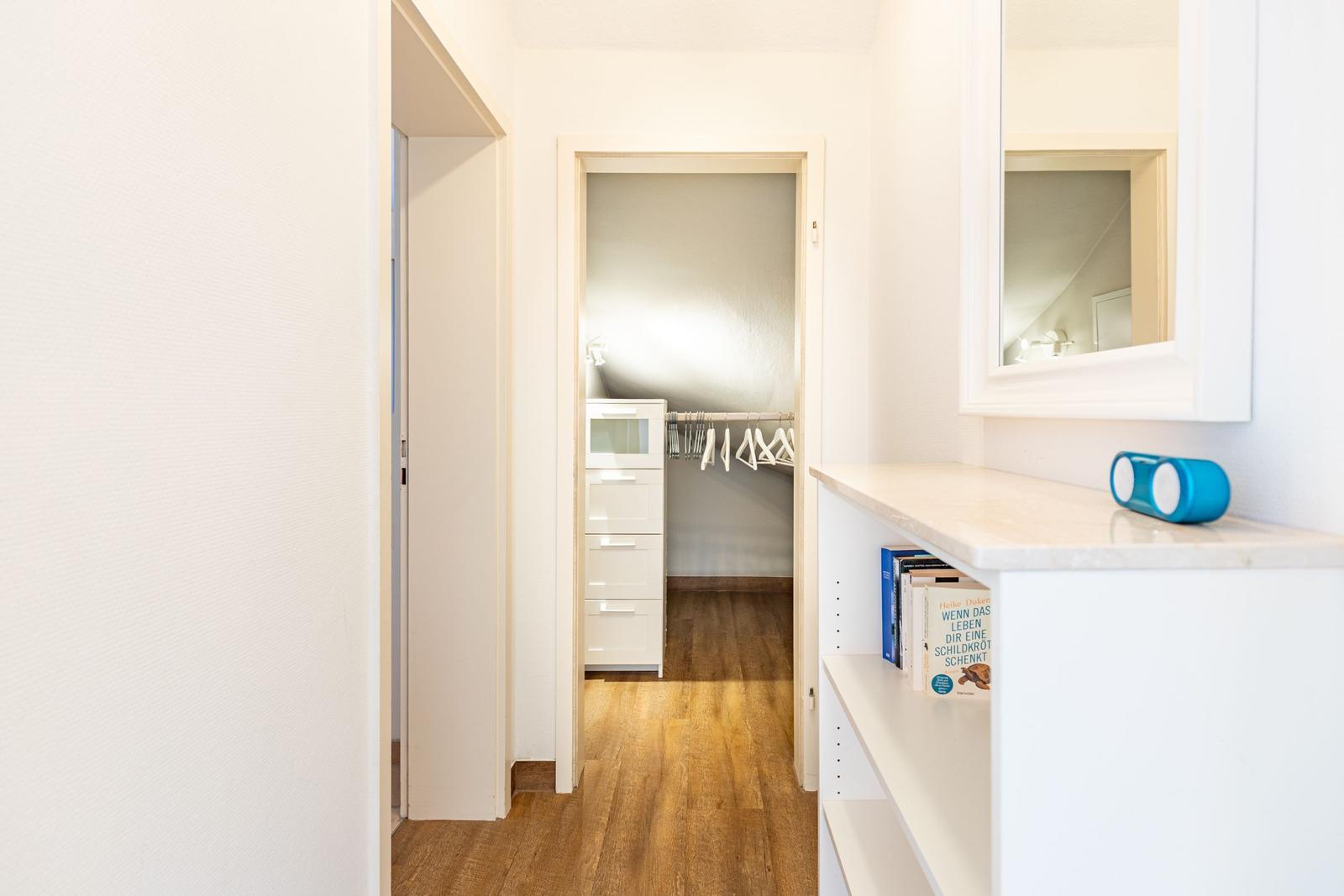 Flur mit Schrank, Spiegel und Bücherregal. Holzboden und weiße Wände.