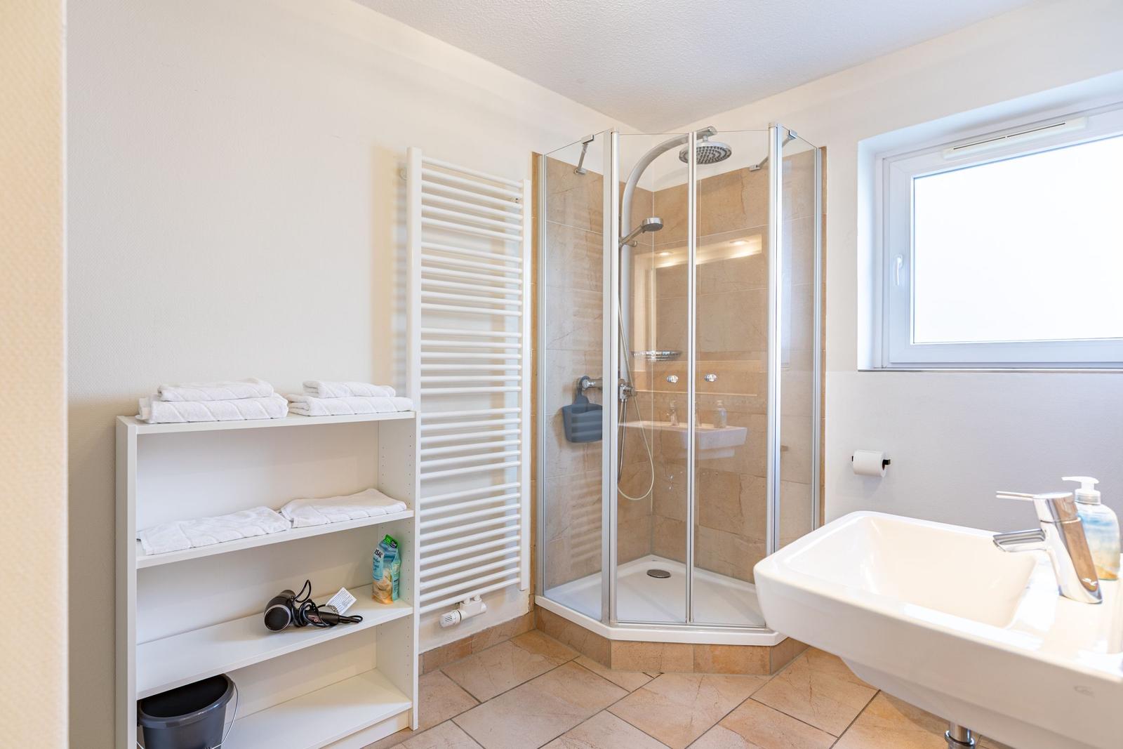 Badezimmer mit Dusche, Waschbecken und Regal mit Handtüchern.