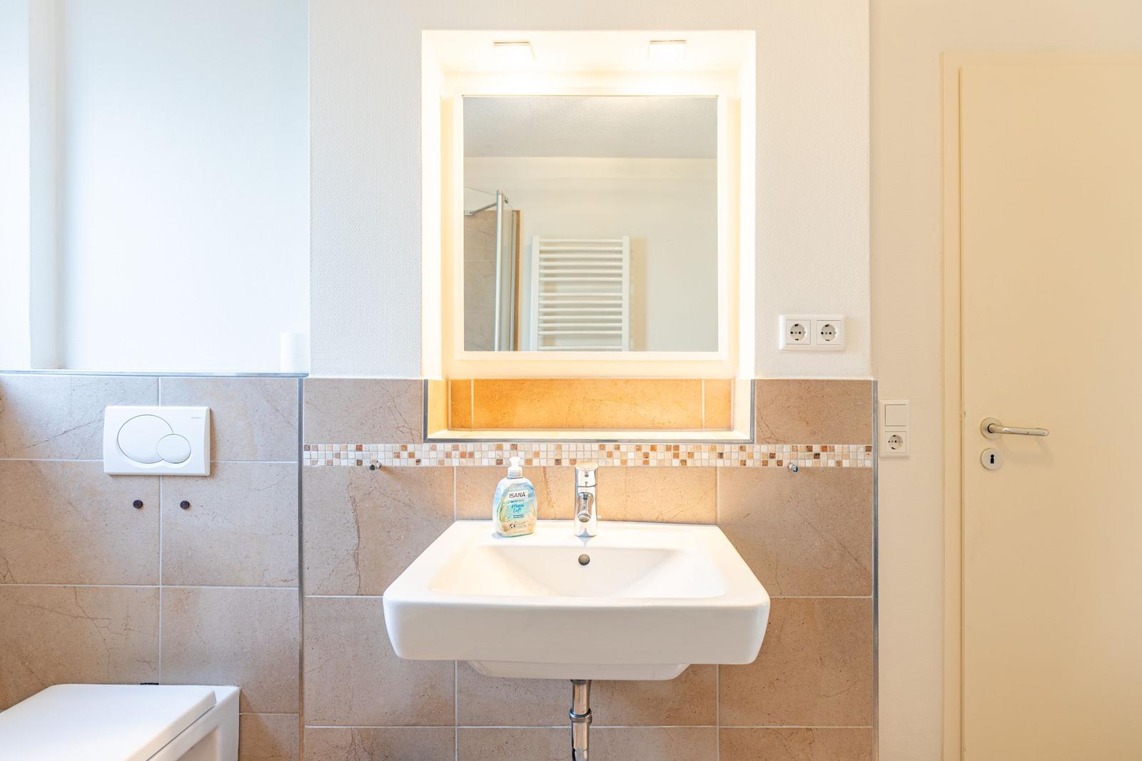 Bad mit Waschbecken, Spiegel und Toilette. Wandverkleidung aus Steinfliesen.