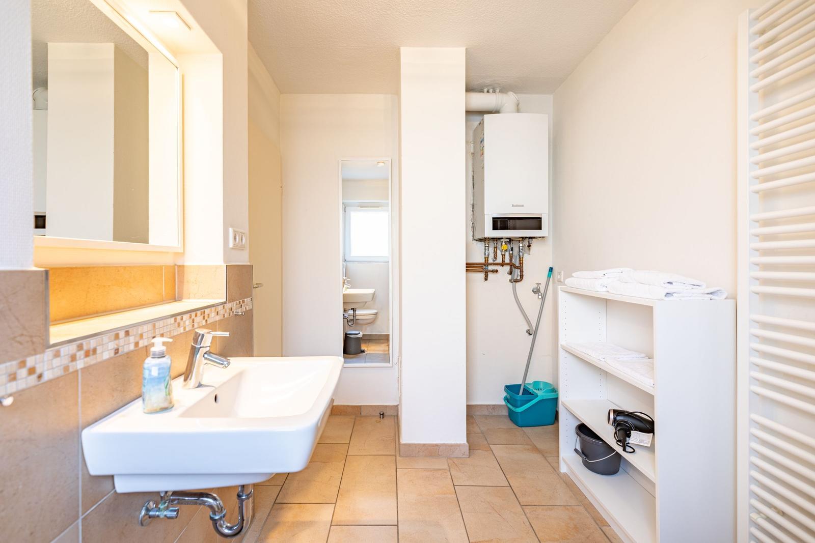 Badezimmer mit Waschbecken, Spiegel, Dusche und Regal.