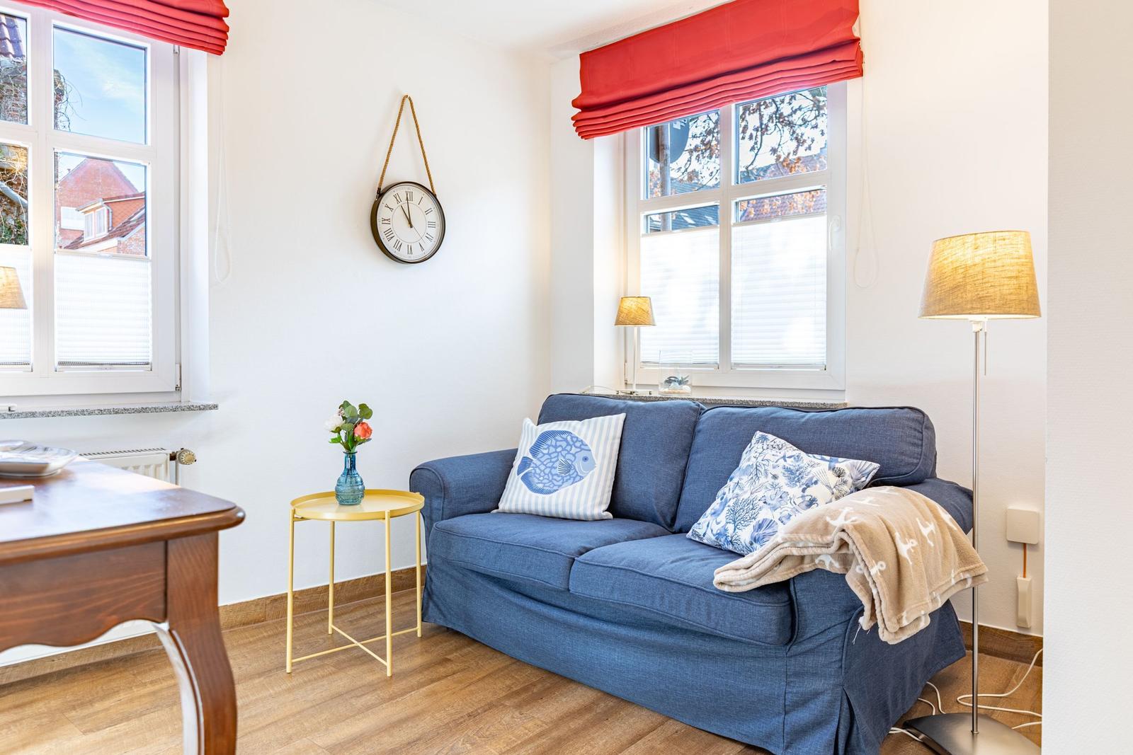 Ein Wohnzimmer mit blauem Sofa, roten Fensterläden und einem Wanduhr.