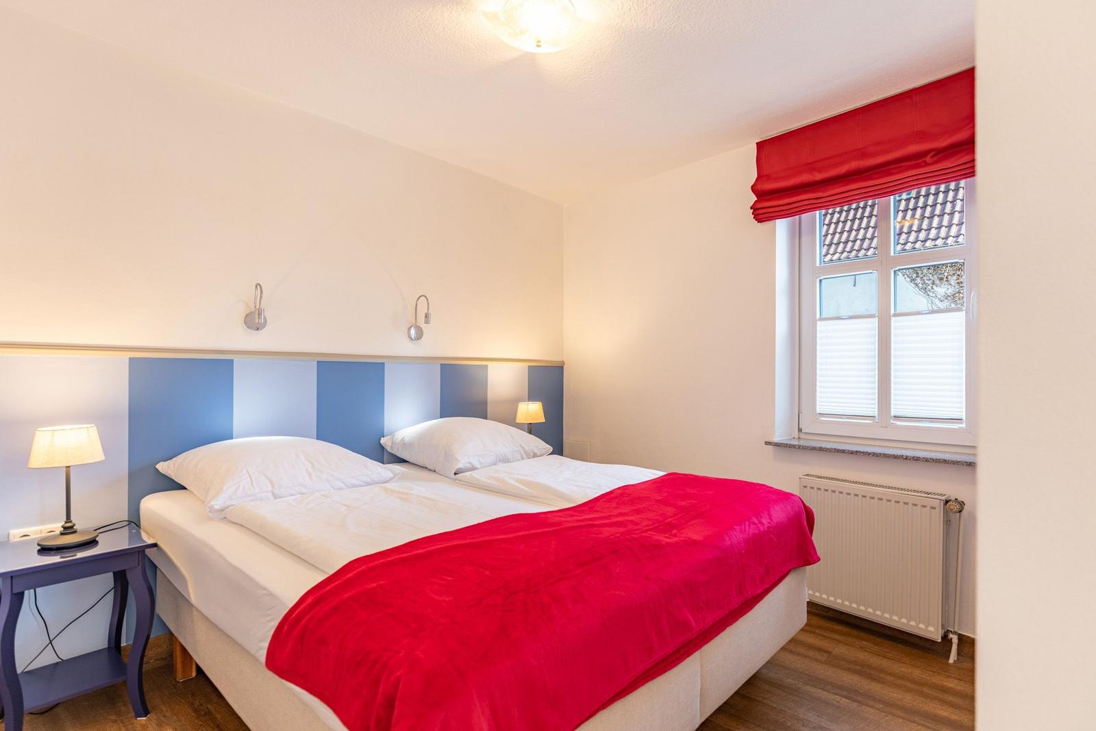 Schlafzimmer mit Doppelbett, rotem Deckenbezug und Fenster mit rotem Rollladen.