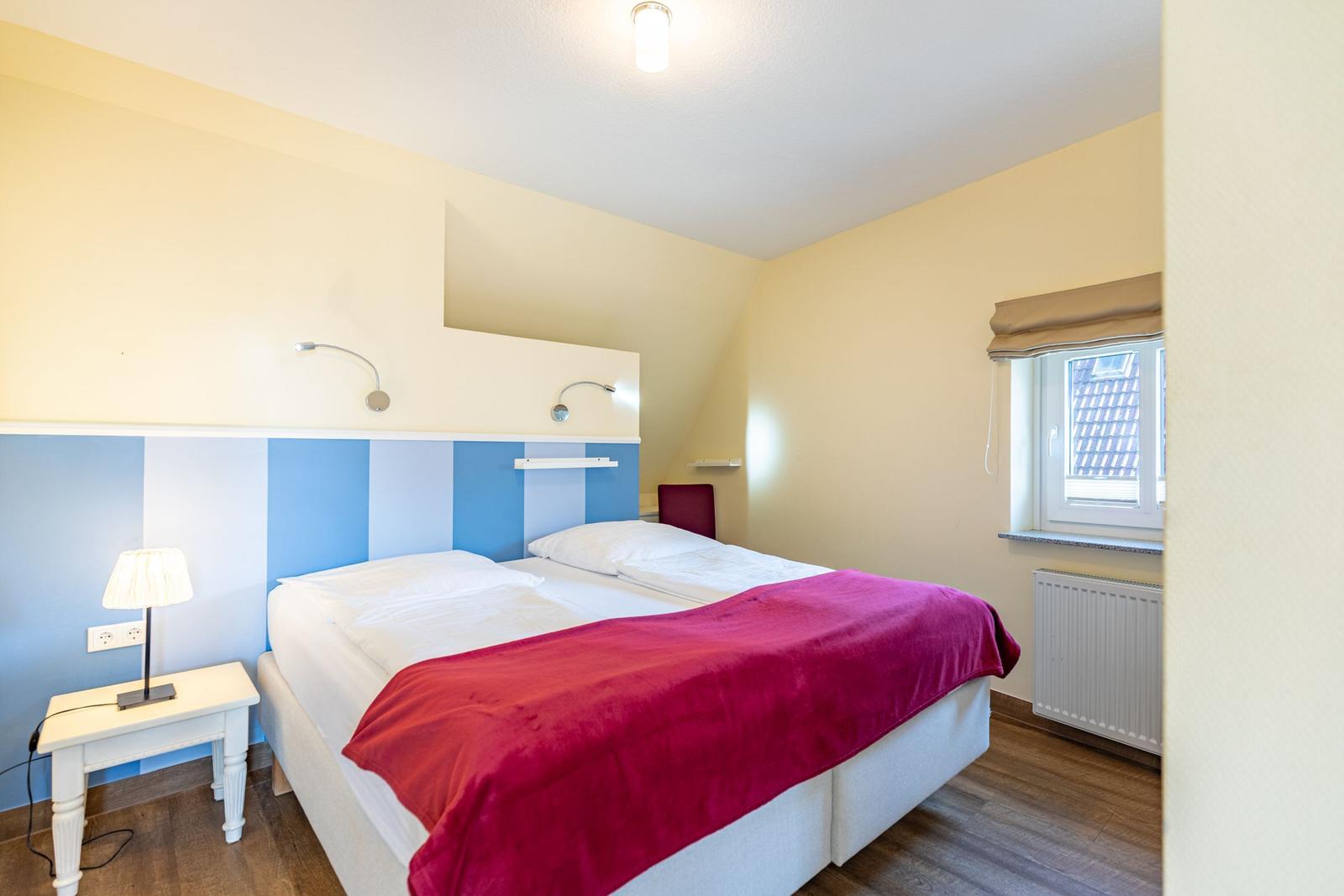 Schlafzimmer mit Doppelbett, Nachttisch und Fenster. Wandgestaltung in Blau-Weiß.