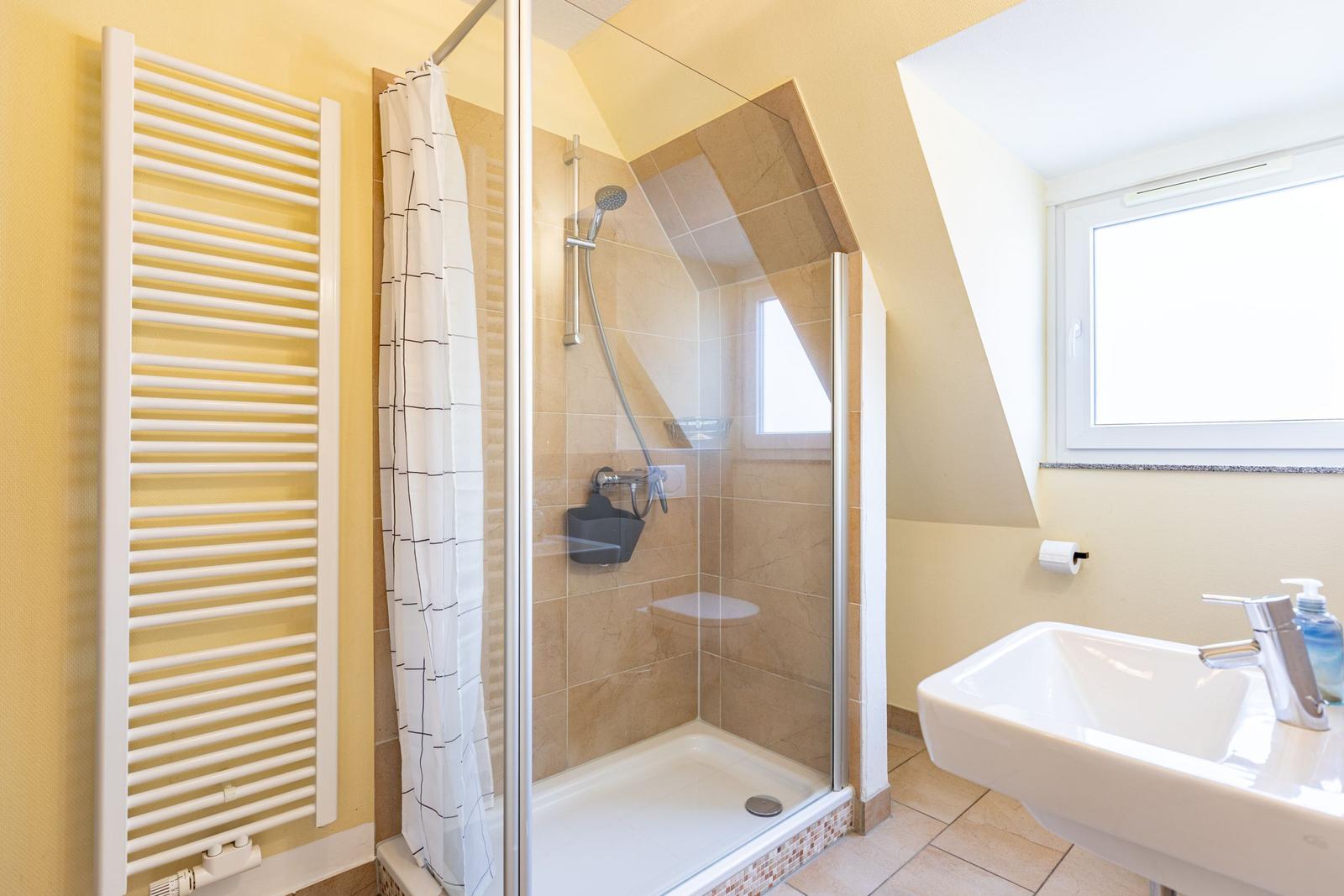 Bad mit Dusche, Waschbecken und Heizkörper an der Wand.
