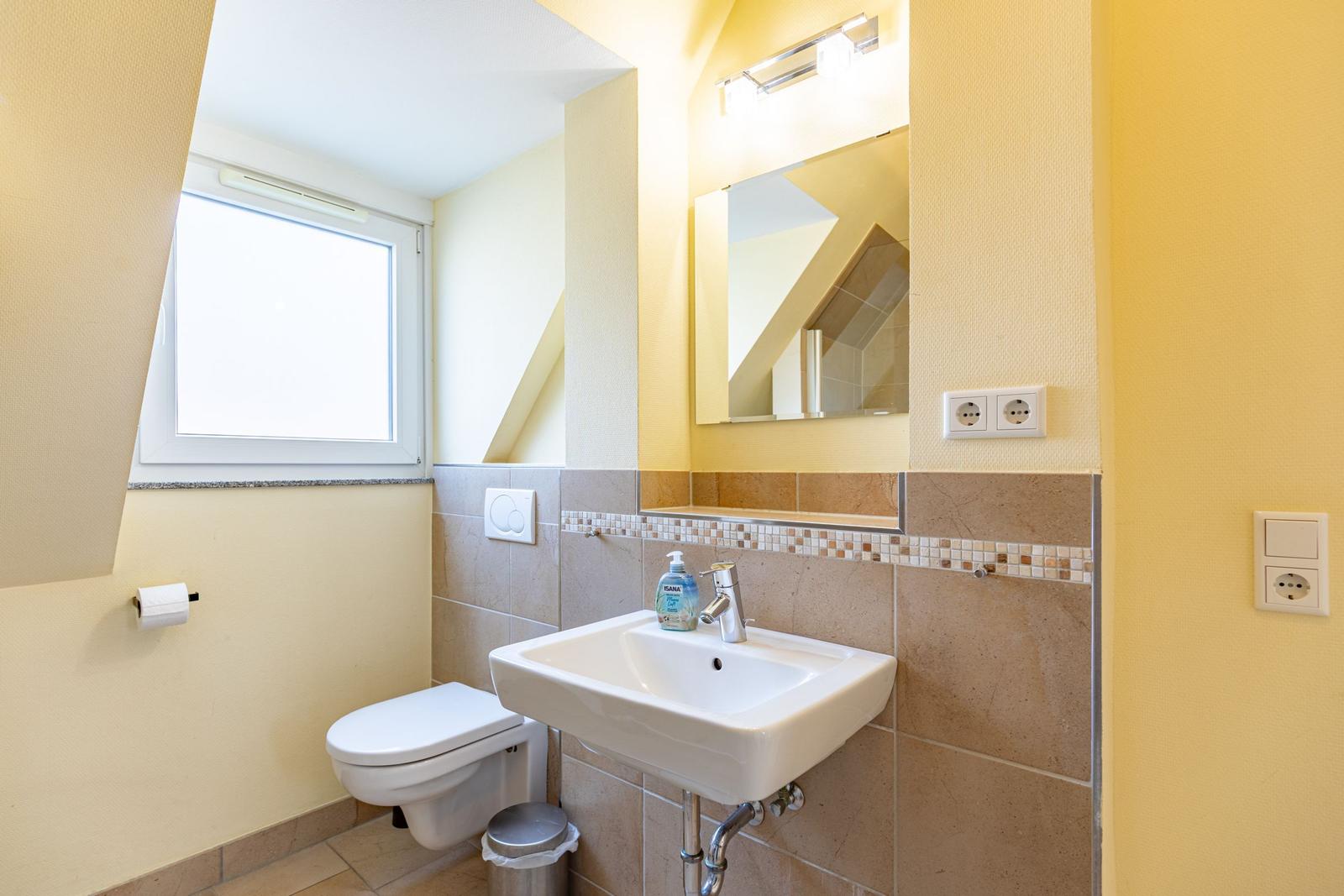 Badezimmer mit Waschbecken, Spiegel, Toilette und Fenster.