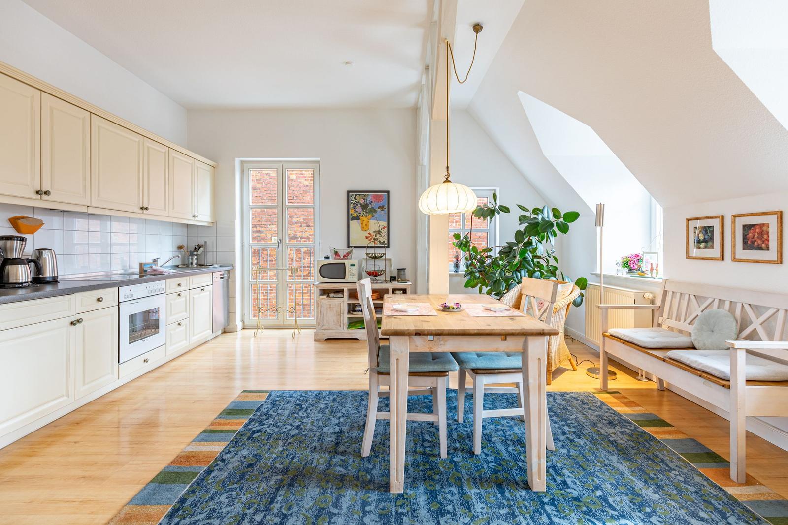 Küche mit Essbereich unter Dachschrägen. Holztisch, Stühle, Sofa und Pflanzen sind sichtbar.