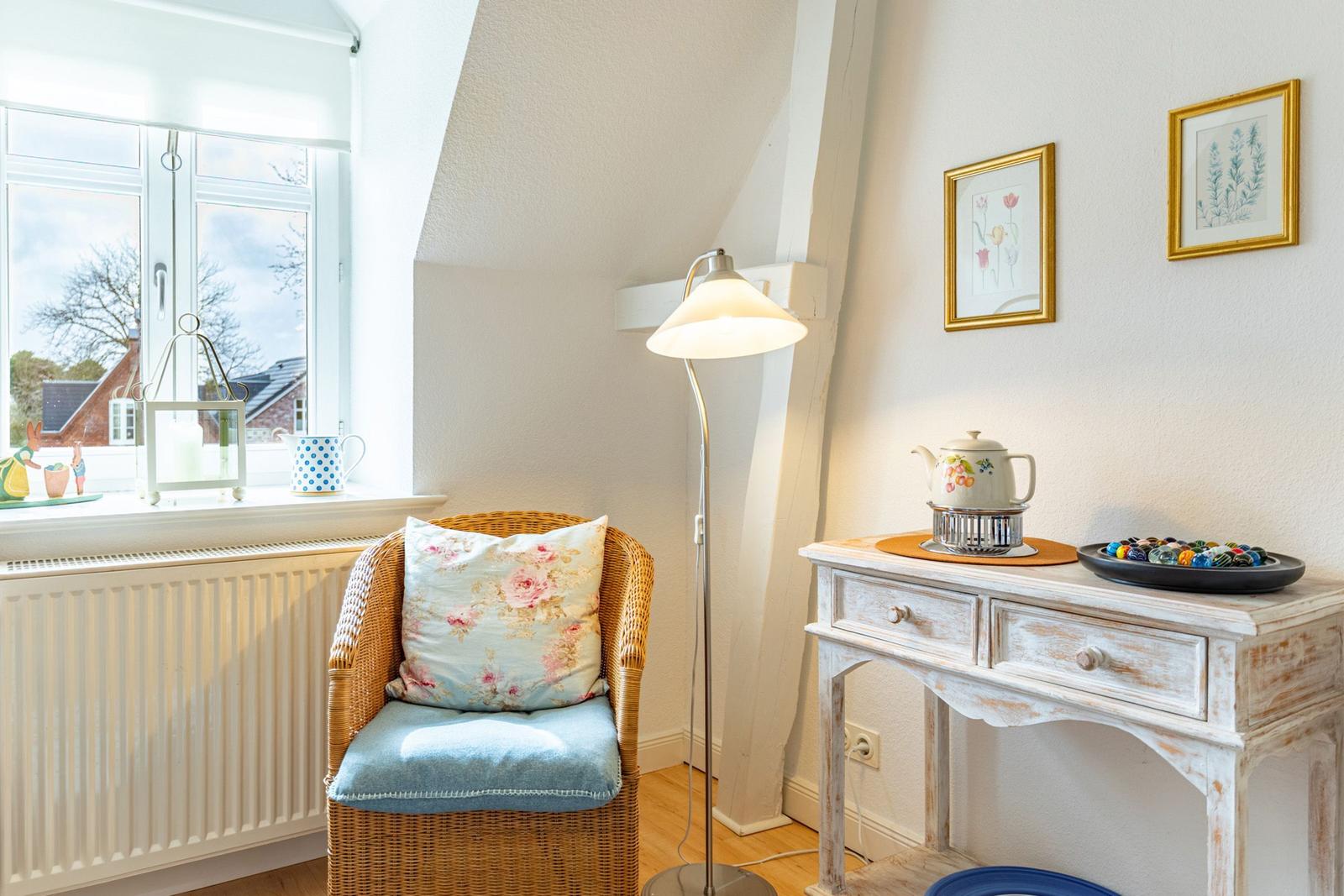 Wohnzimmer mit Sessel, Stehlampe und Schreibtisch. Fenster mit Blick auf Außen.