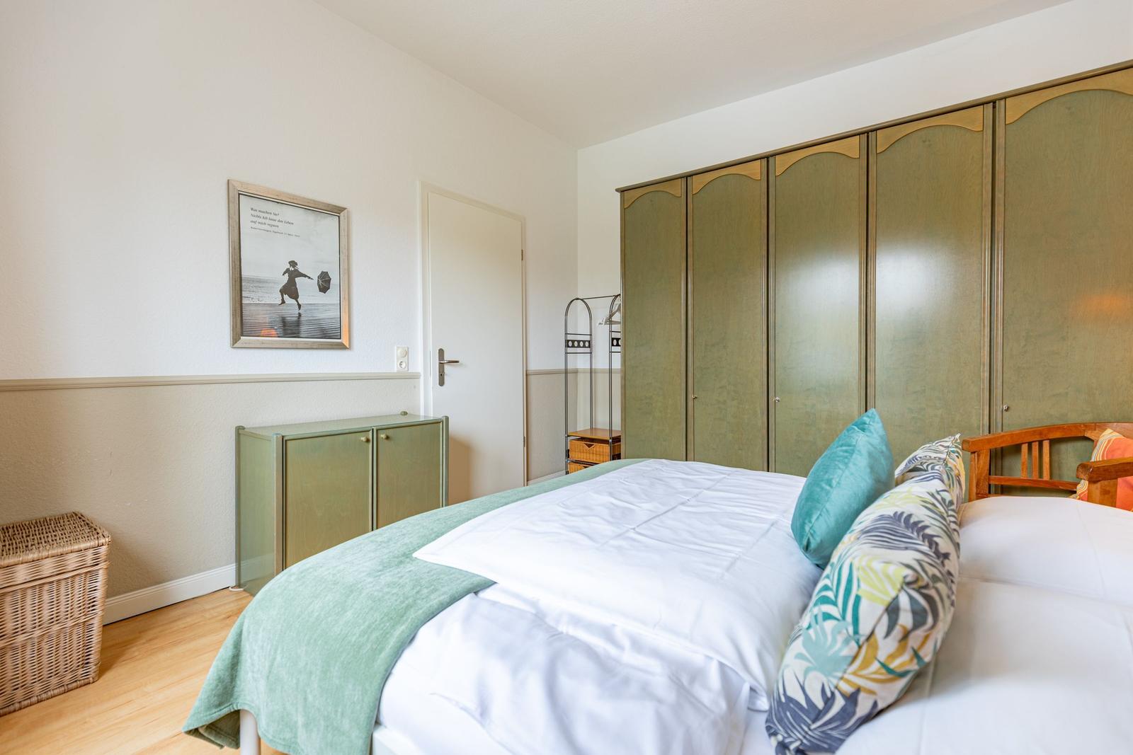 Schlafzimmer mit Bett, Kleiderschrank und Wandbild.