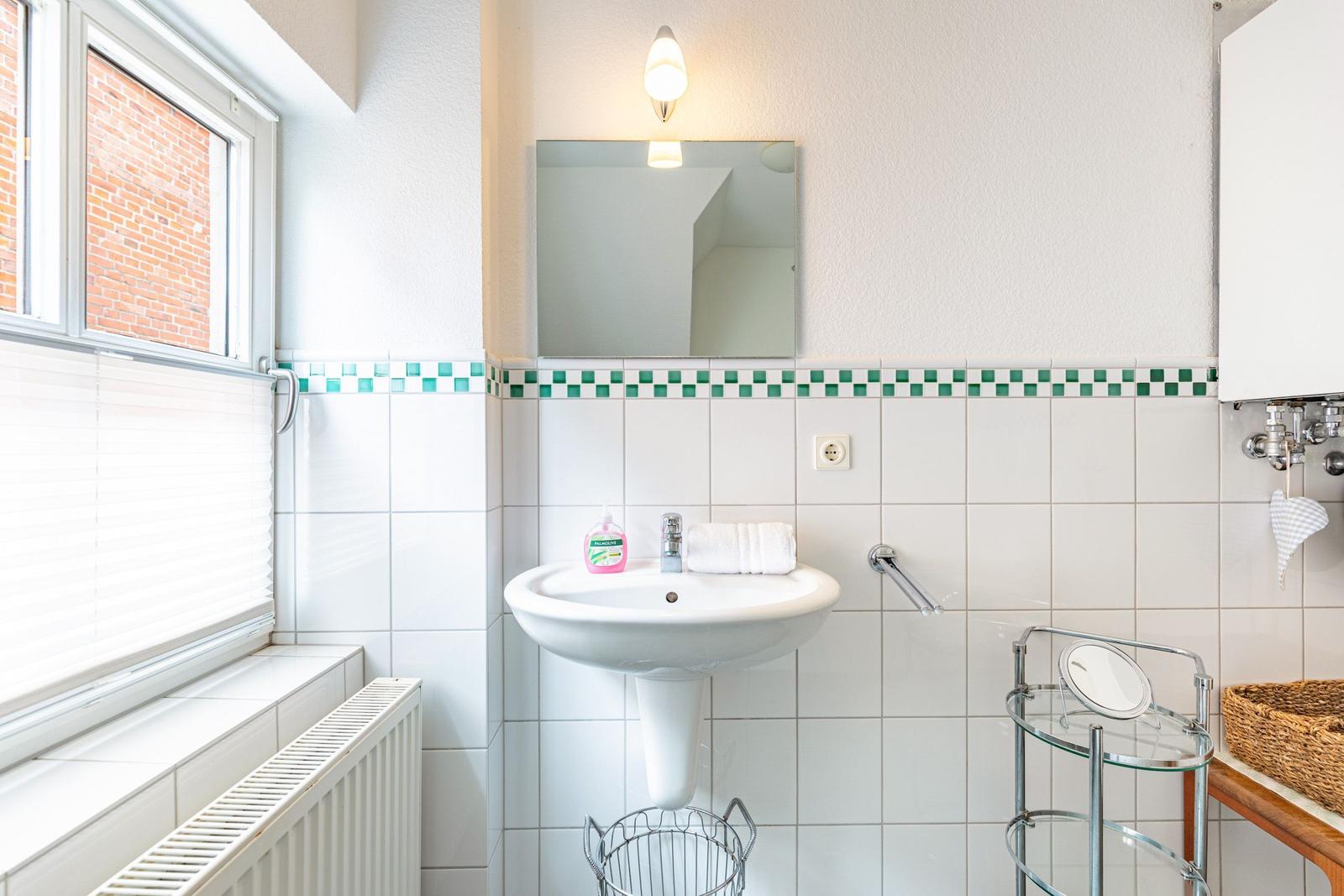 Badezimmer mit Waschbecken, Spiegel, Fenster und Handtuchhalter.