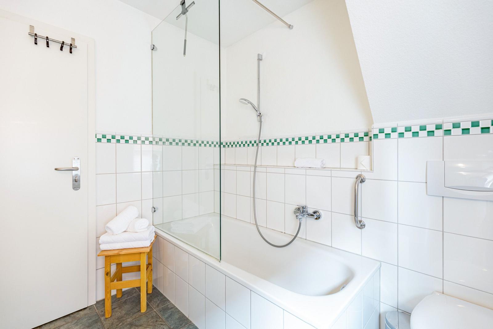 Badezimmer mit Badewanne, Dusche und Toilette. Weiße Fliesen mit grüner Zierleiste.